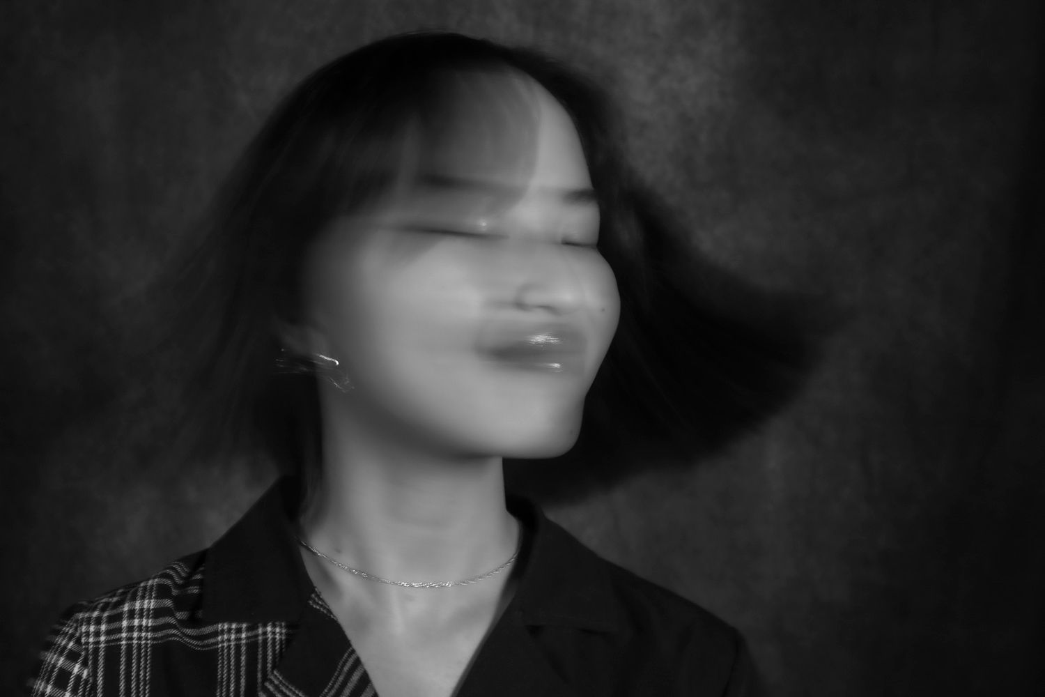 Black and white motion blur portrait of a young Asian woman shaking her head, creating a ghostly double exposure effect.