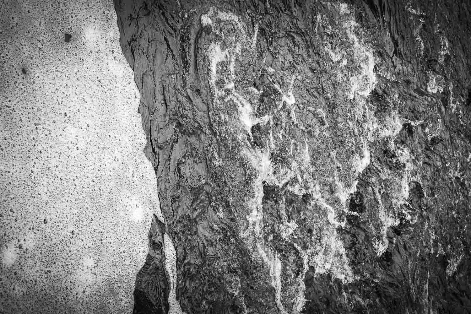 Black and white close-up photograph of contrasting rock textures showing rough granite and smooth wet stone surfaces.