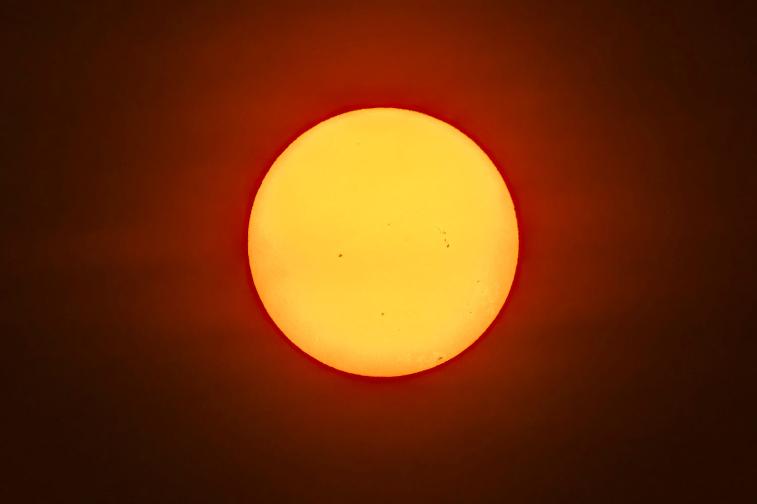 Soleil
Close-up photograph of the sun showing sunspots against a vivid orange and red sky background.