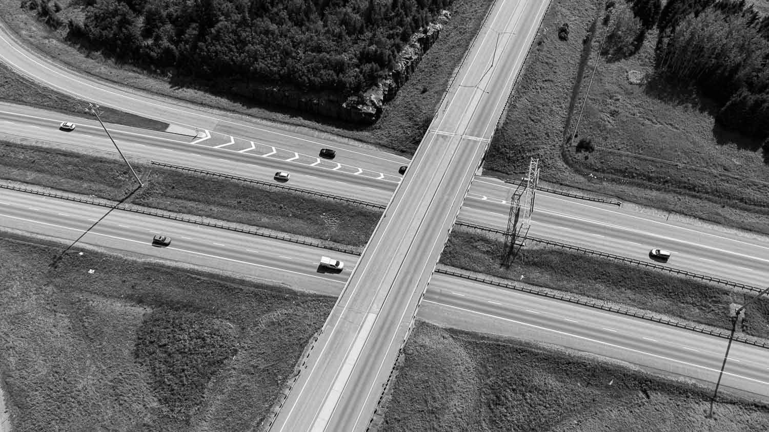 Aerial black and white view of a rural four-way road intersection with passing cars.