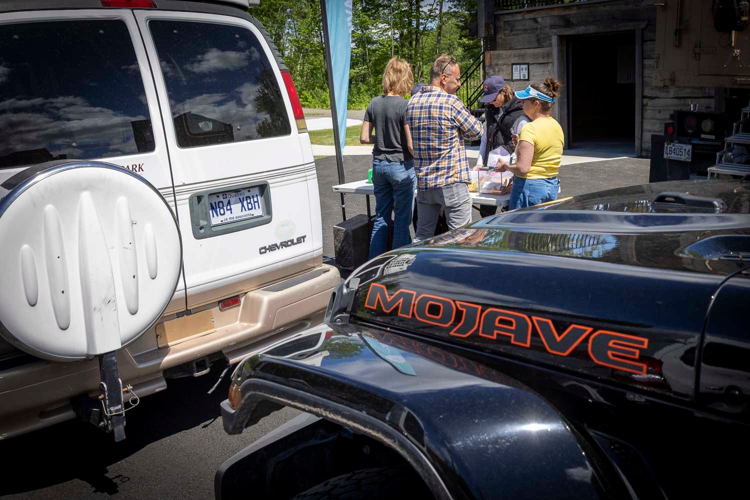 A Chevrolet SUV and Mojave vehicle at an outdoor gathering with people socializing in the background.