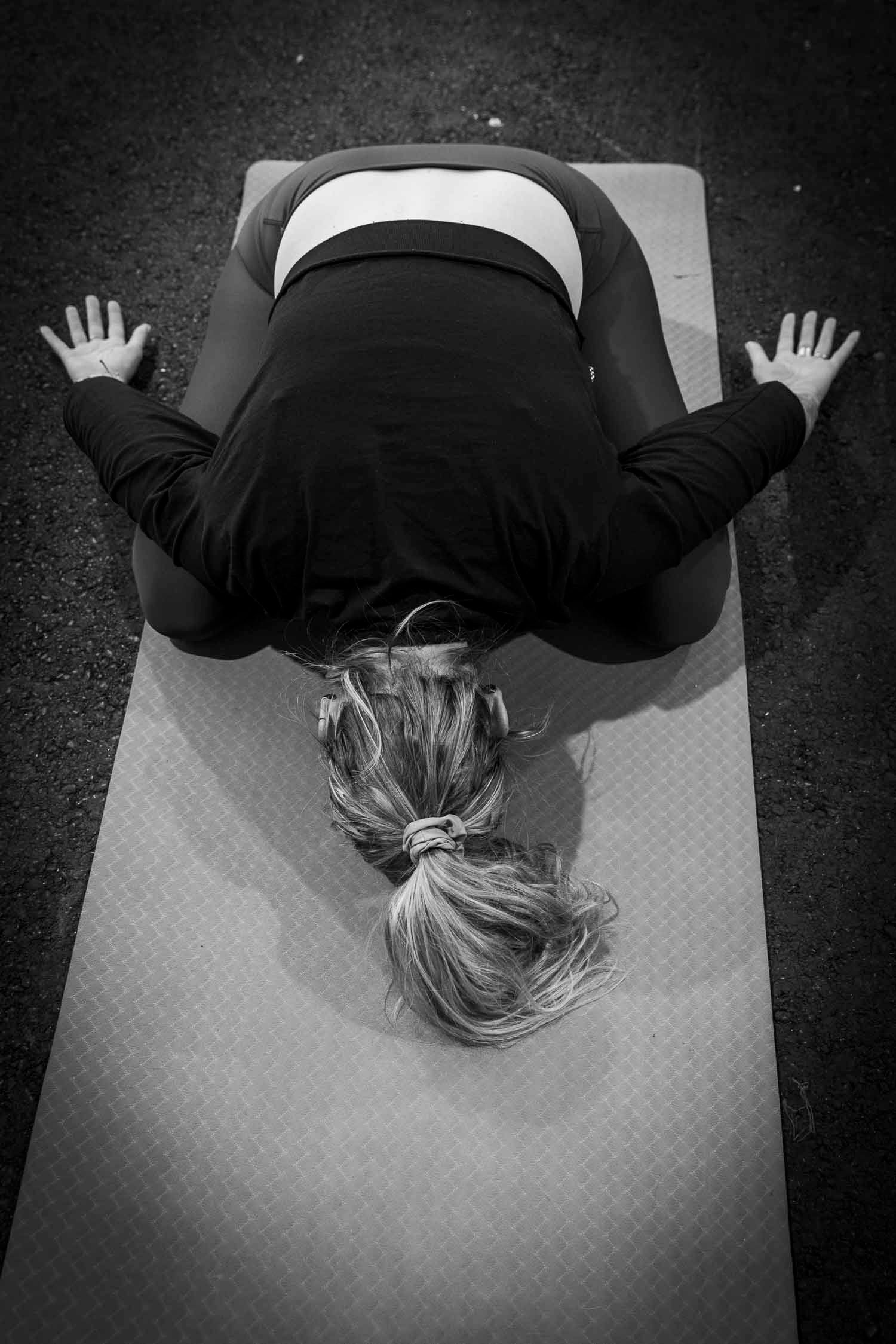 Black and white aerial view of a woman in childs pose on a yoga mat outdoors.