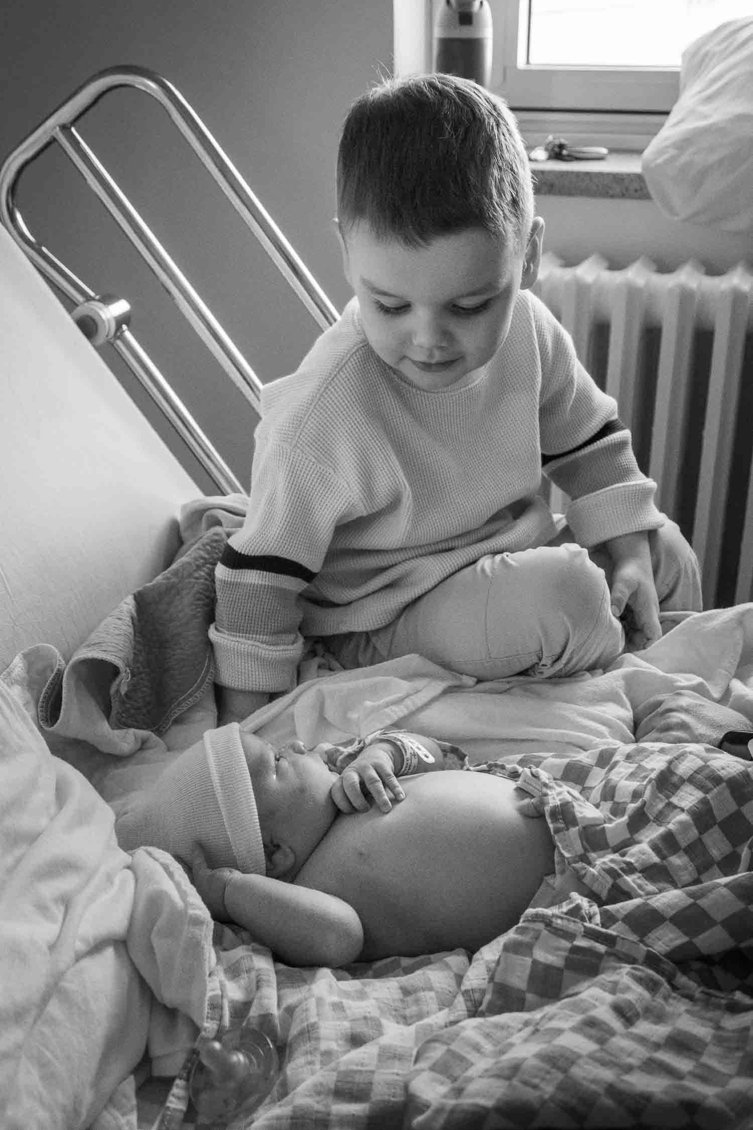 Black and white photo of young boy gently holding a newborn baby in a hospital room.