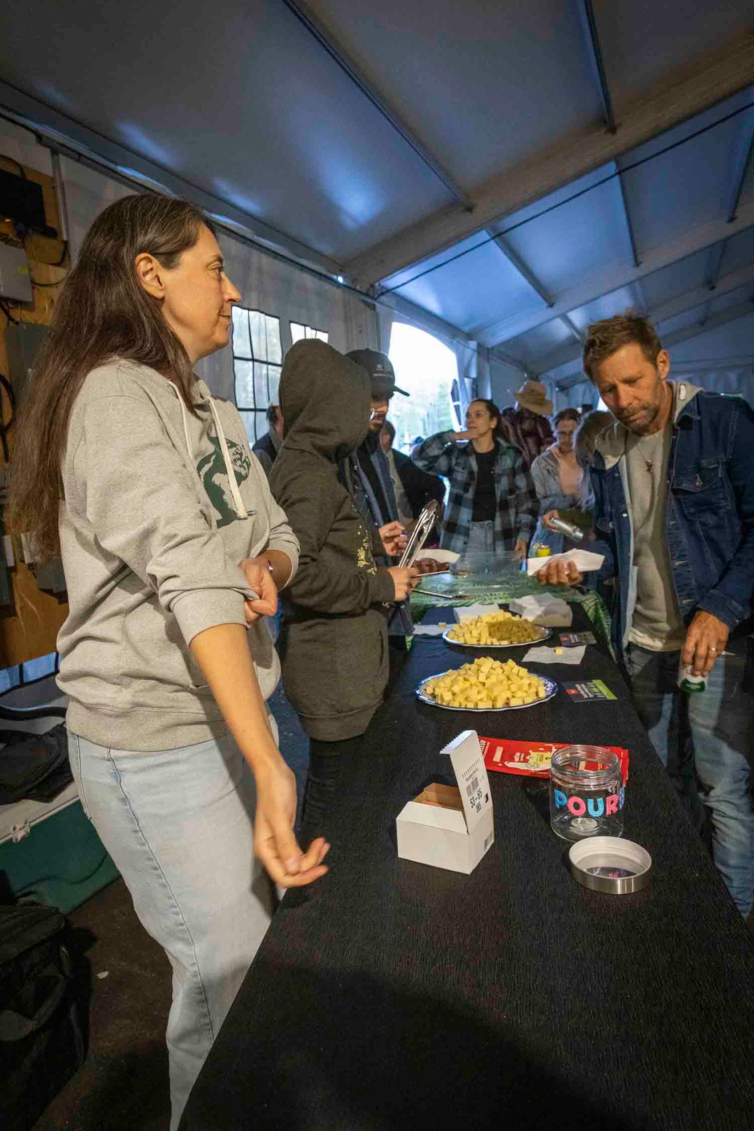 People gathered at an outdoor event tent with snacks on a black table during a community gathering.