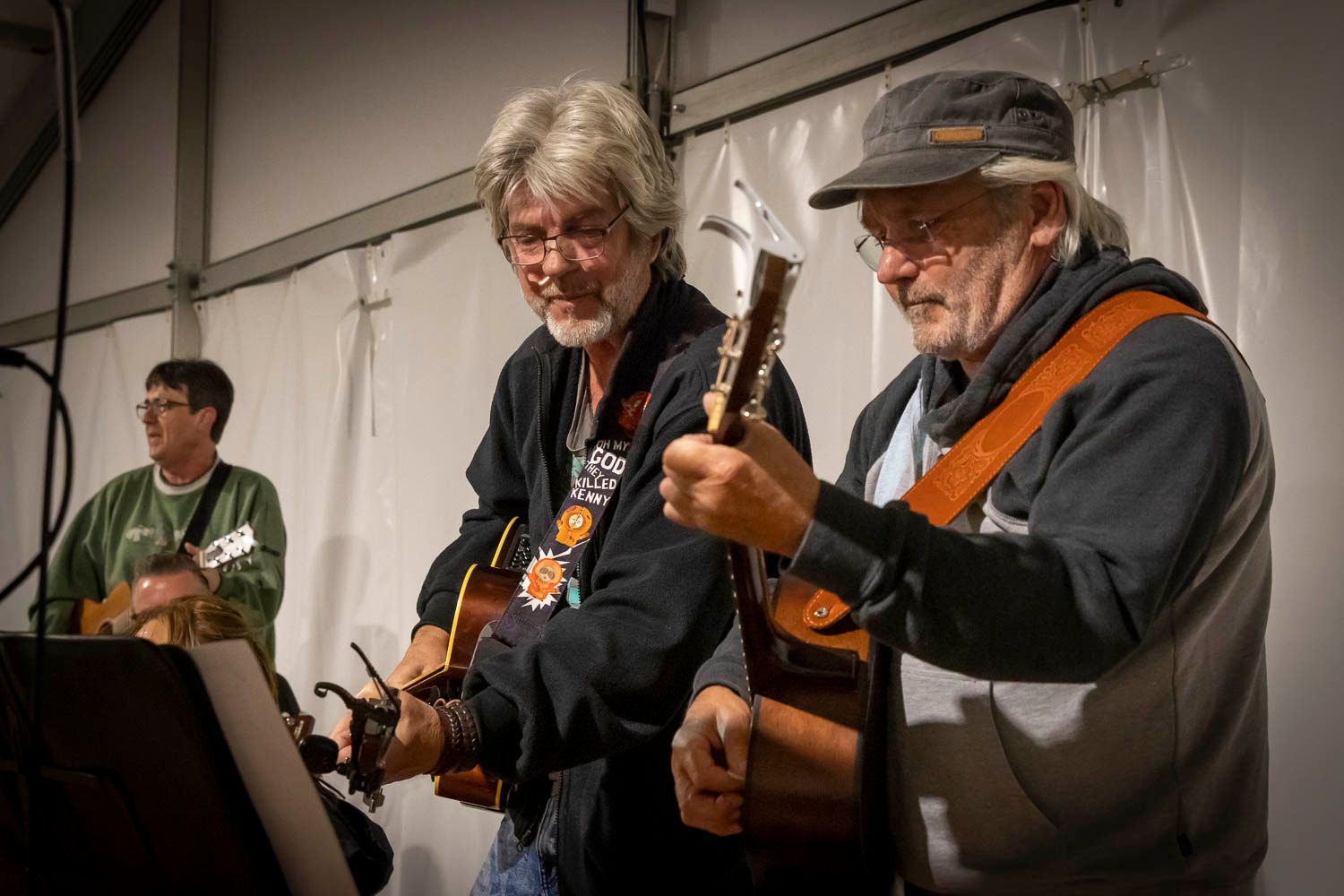 Two older men playing acoustic guitars together on stage at an outdoor music performance.