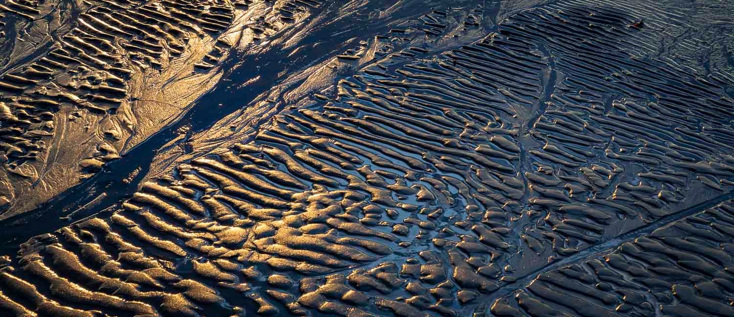 Close-up aerial view of rippled wet sand patterns with golden light at low tide.