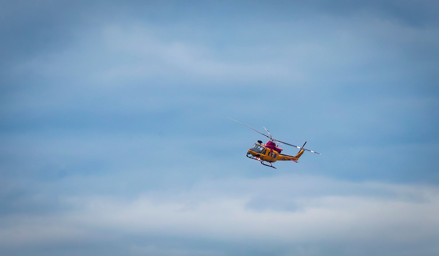 A bright yellow and red helicopter flying low against a cloudy sky.