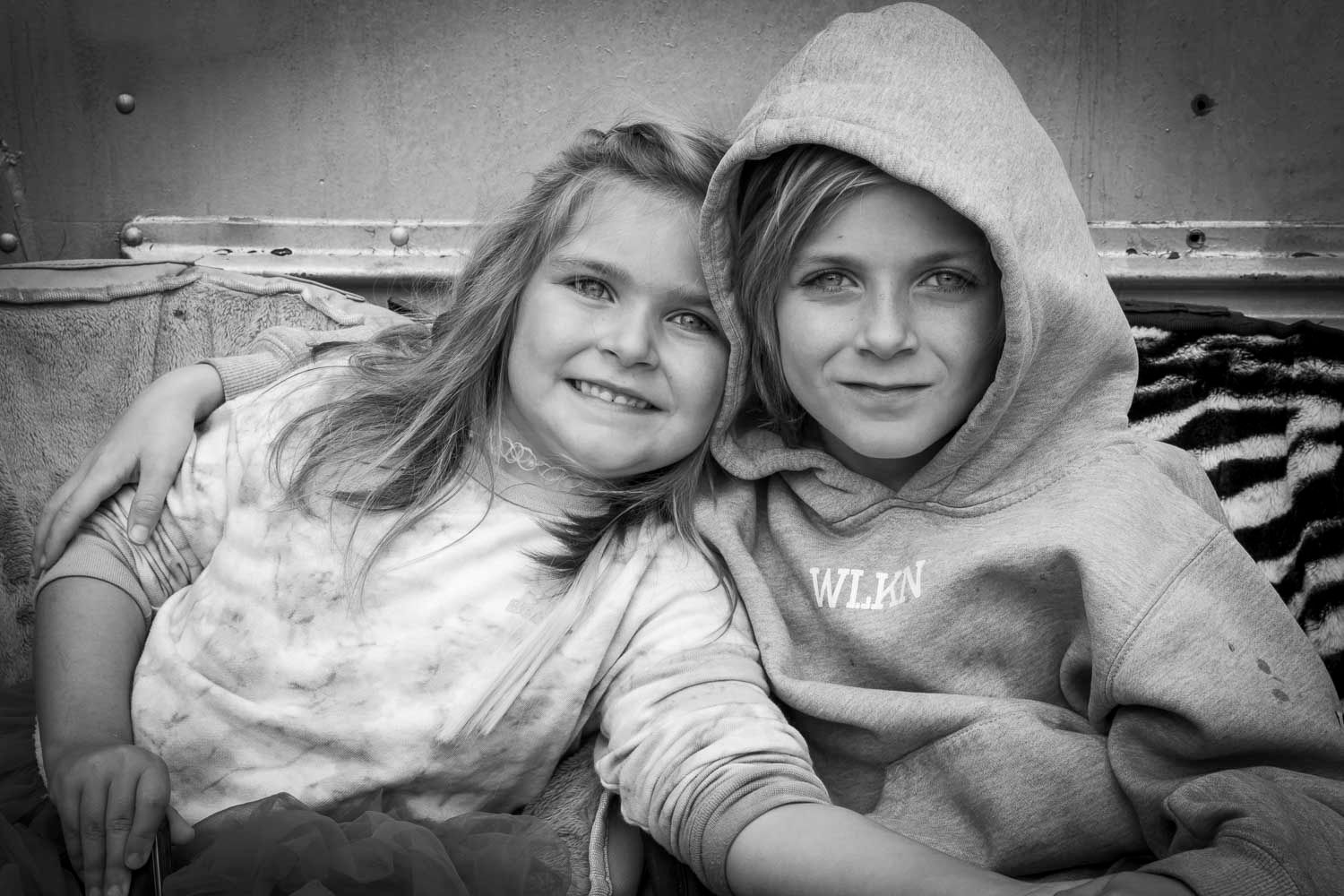 Frère et soeur, vanlife, Québec, Canada
Black and white photo of two smiling children cuddling together on a couch, wearing casual hoodies.