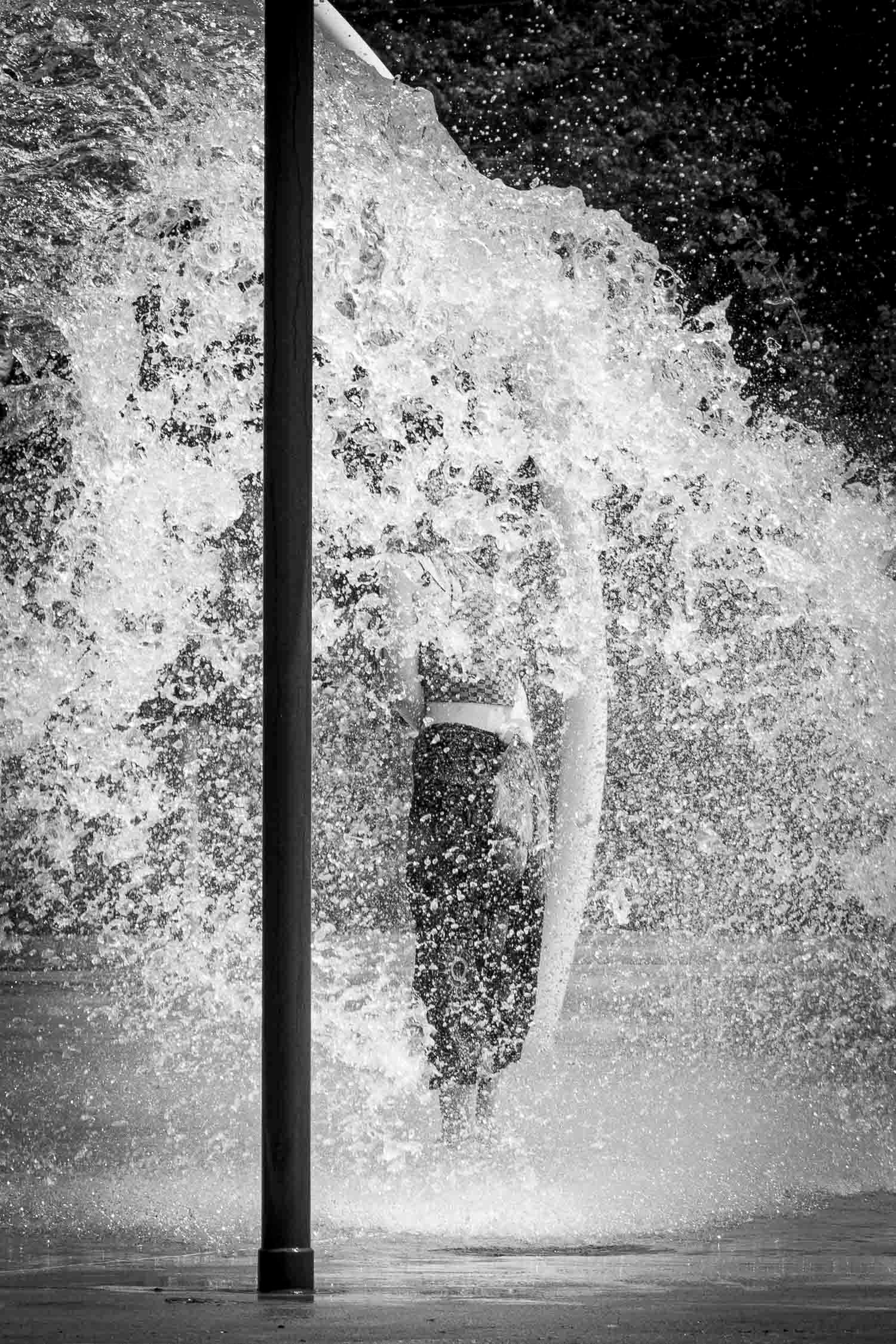 Black and white dramatic shot of a person standing beneath a powerful cascading waterfall outdoors.