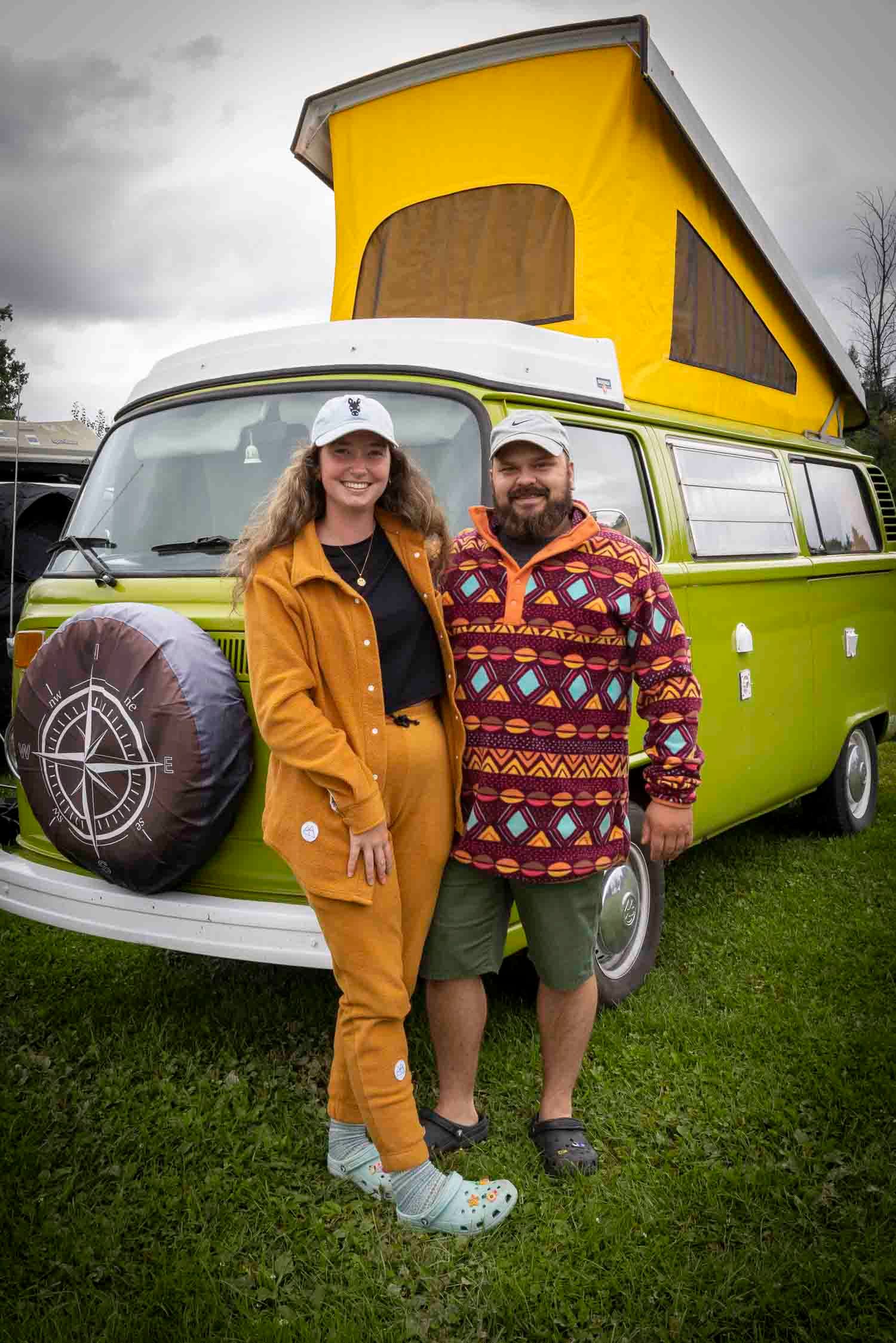 Couple smiling in front of a vintage green and yellow Volkswagen camper van with pop-top roof.