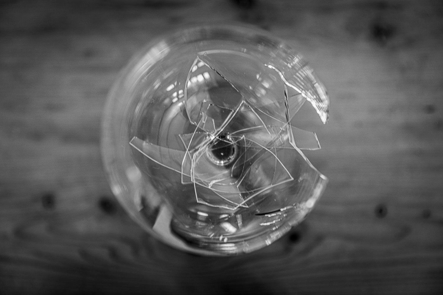 Black and white top-down view of a broken light bulb in a glass on wood.
