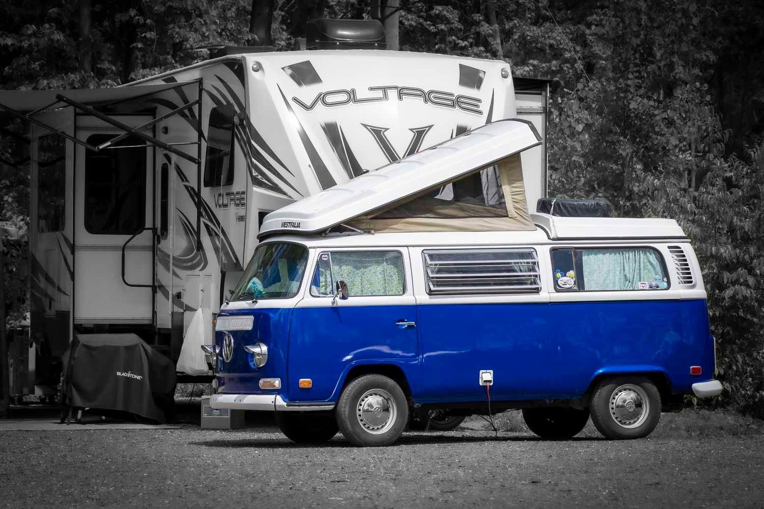 Classic blue Volkswagen camper van parked beside a white Voltage RV in a campground.