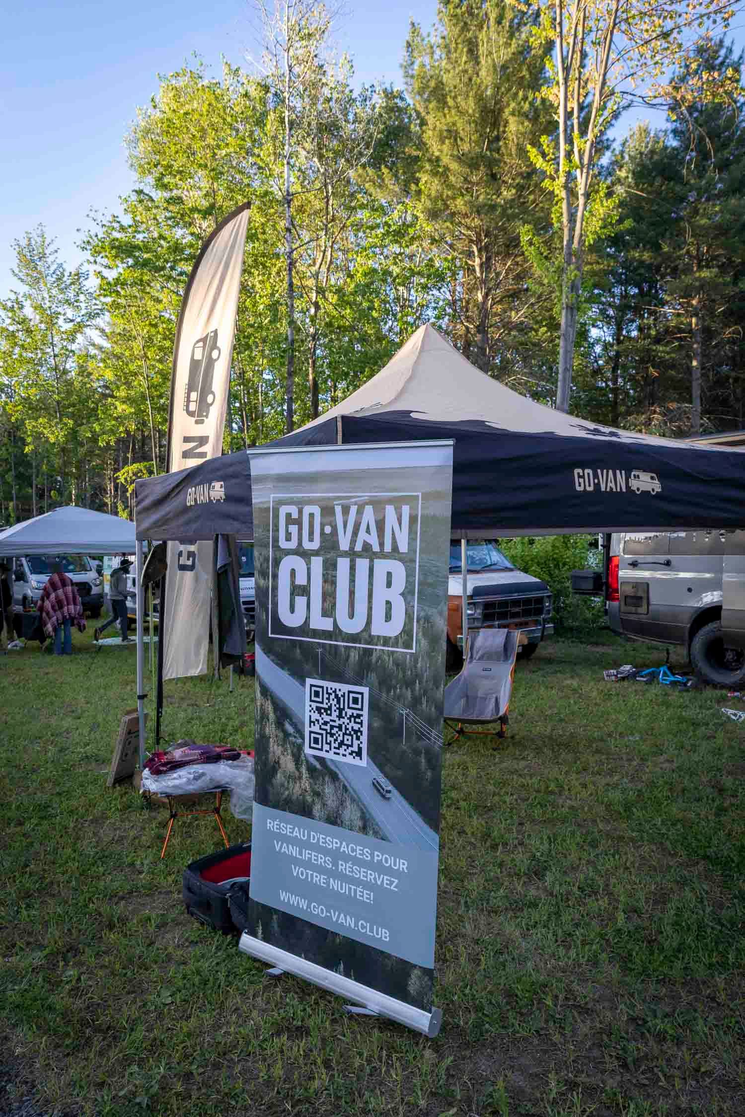 Go-Van Club promotional banner and tent setup at an outdoor camping event surrounded by trees.