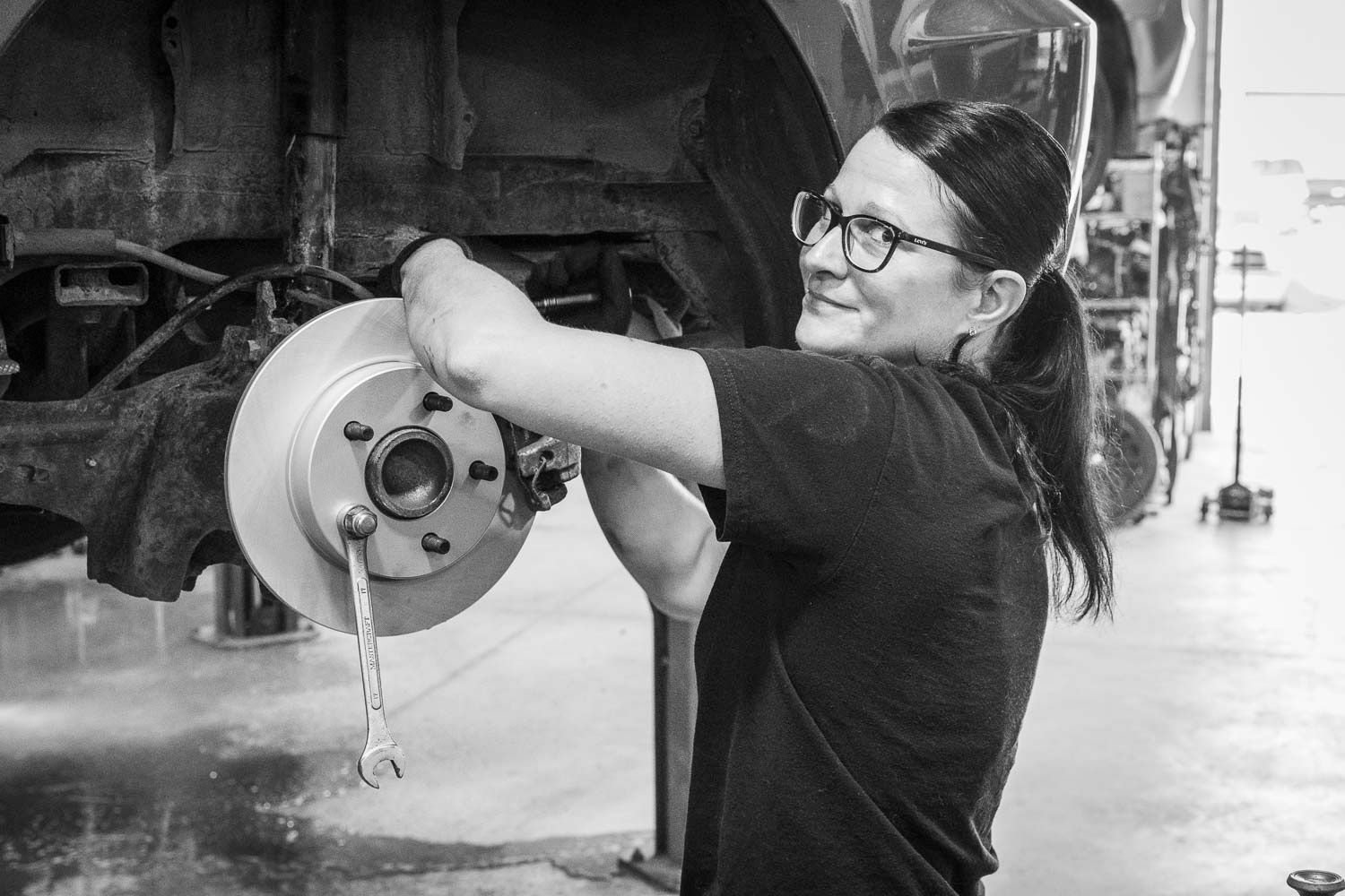 A smiling woman mechanic works on a car brake rotor in a garage in black and white.