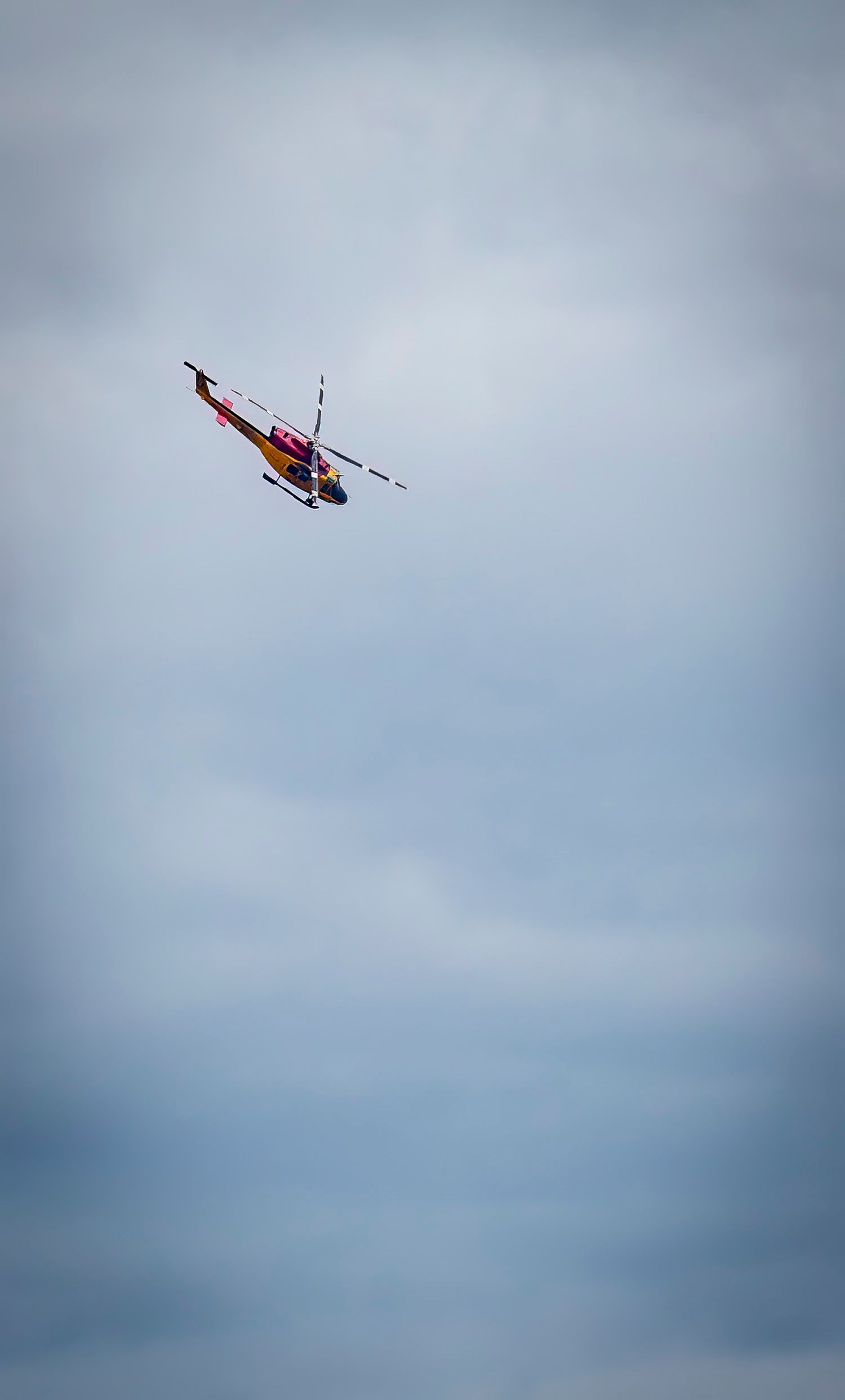 A colorful red and yellow helicopter banking sharply against cloudy skies.