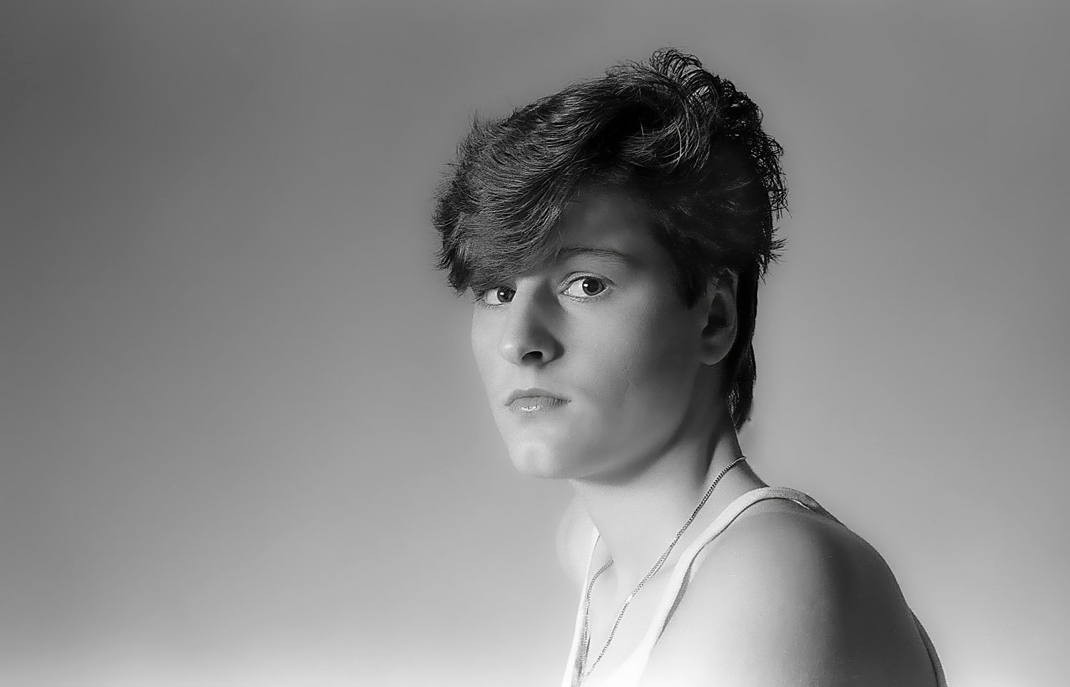 Black and white portrait of a young person with short tousled hair wearing a white tank top against a gray background.