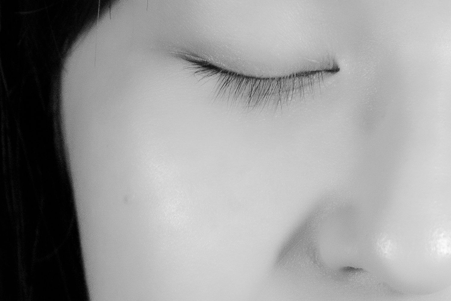Close-up black and white portrait of a woman with closed eyes and long eyelashes.
