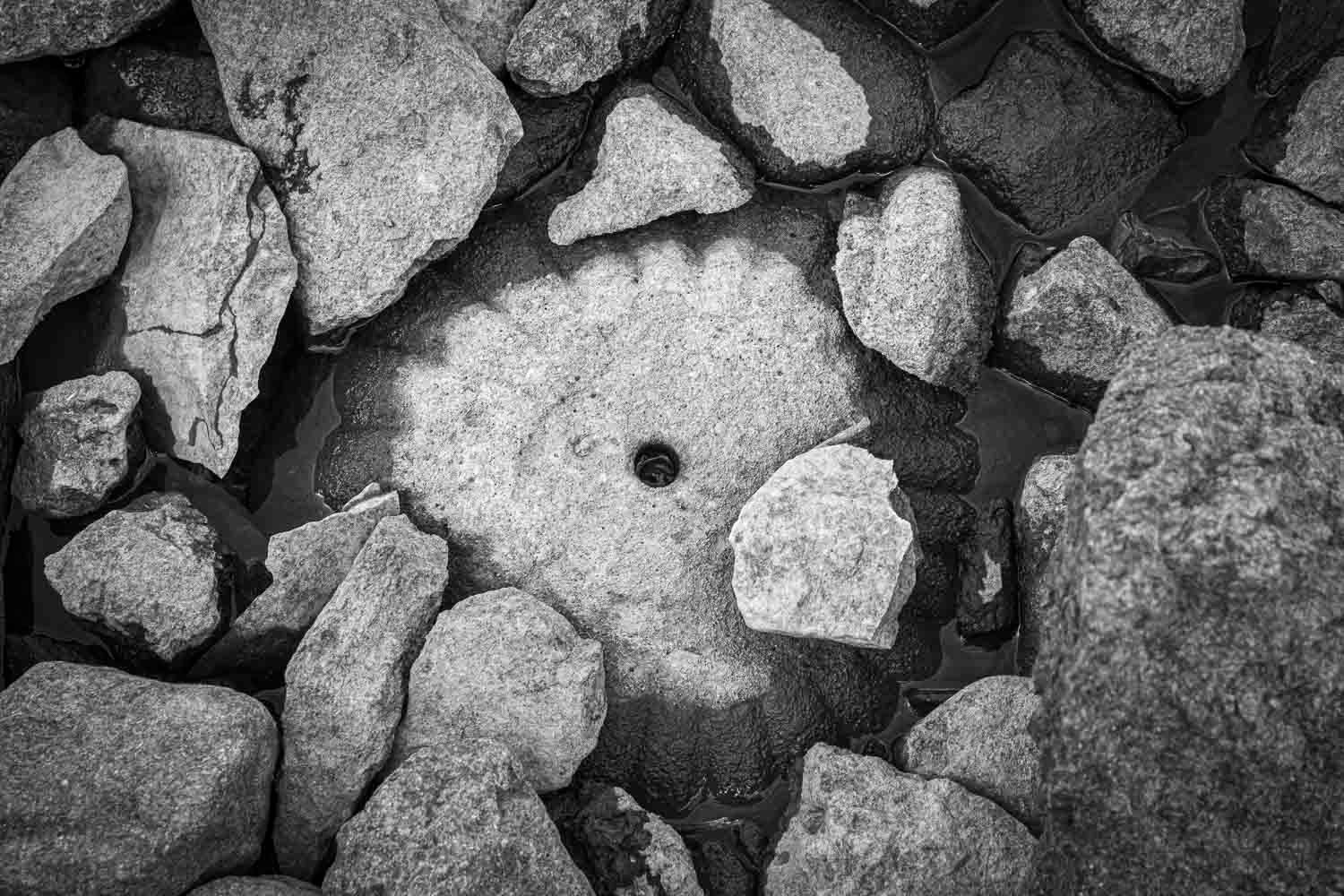 Aerial black and white view of rugged rocks surrounding a circular stone with a small hole in the center.