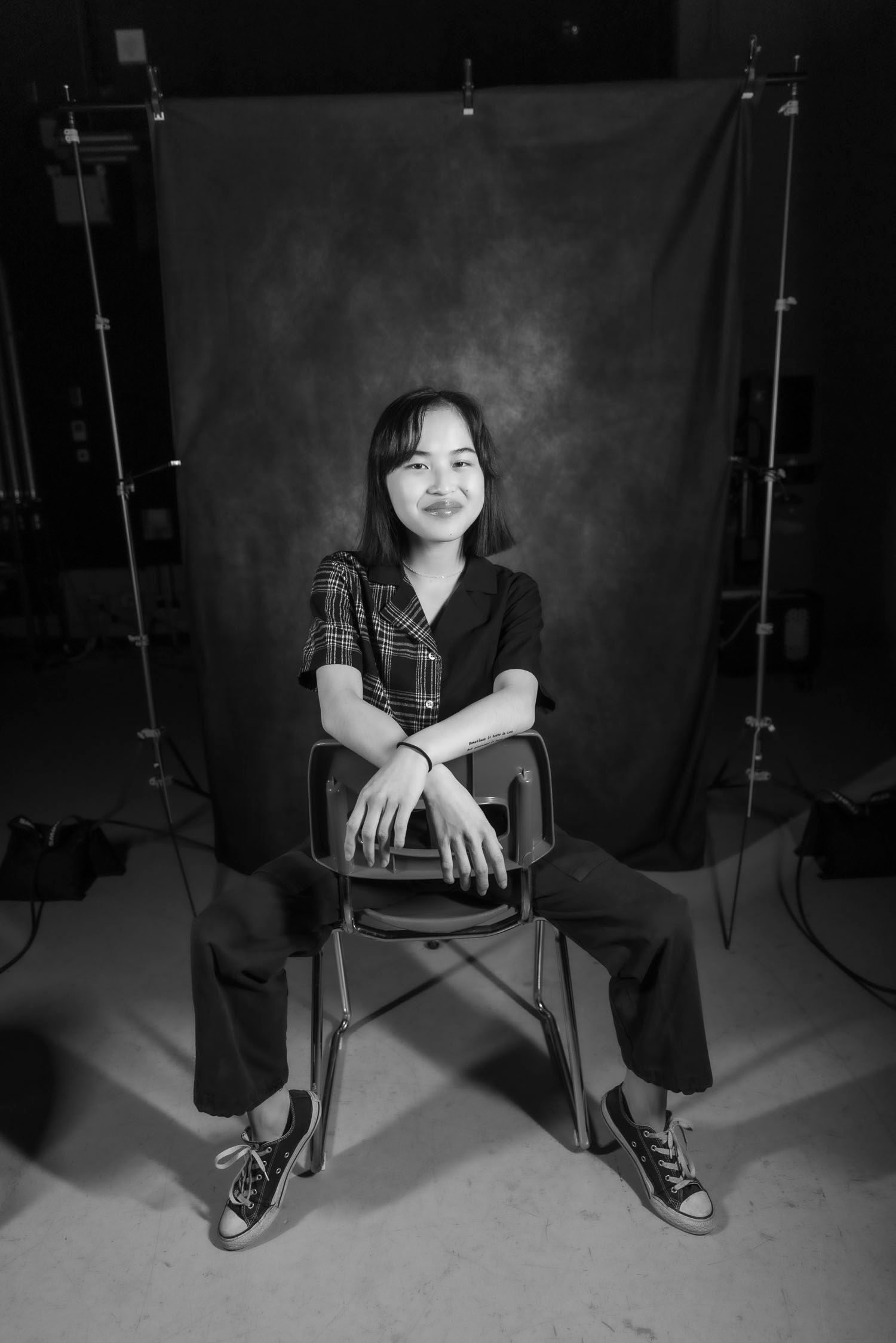 Young Asian woman sitting on chair in photography studio, black and white portrait with studio lights.