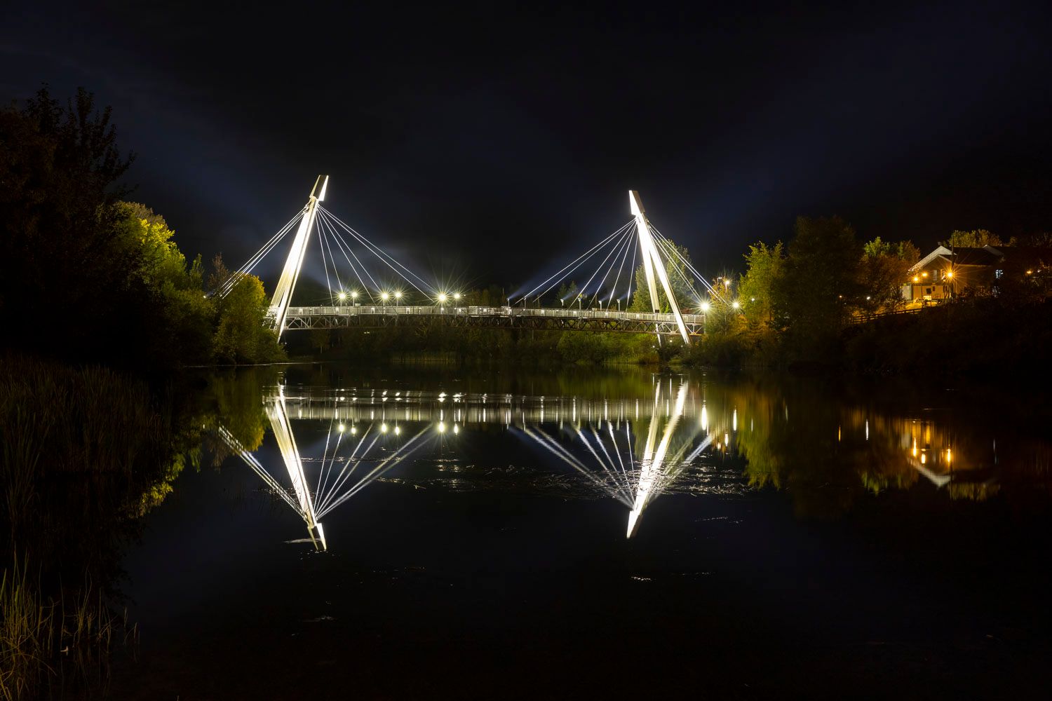 Pont Rivière au sable, de nuit.
Illuminated cable-stayed bridge reflecting on calm river water at night with glowing lights and dark sky.