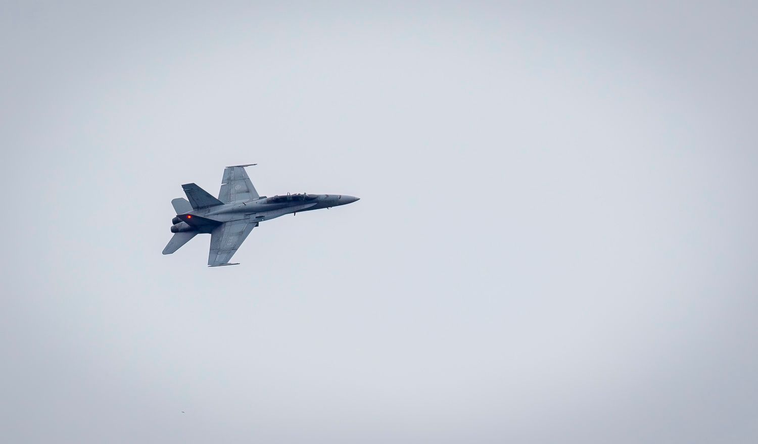 Single CF-18 Hornet fighter jet banking sharply against a pale grey overcast sky.