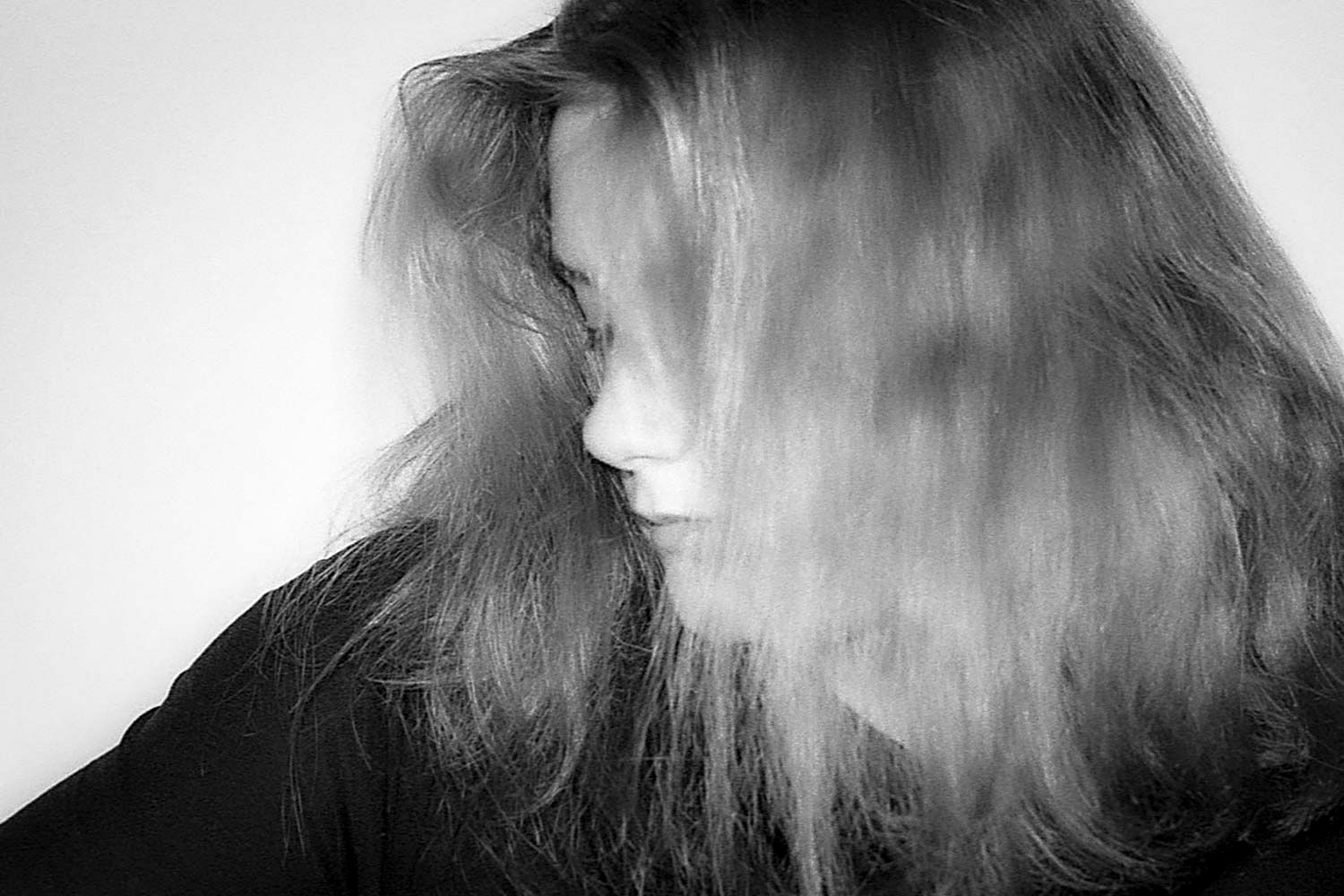 Black and white portrait of a woman with long hair blowing across her face, creating a moody motion blur effect.