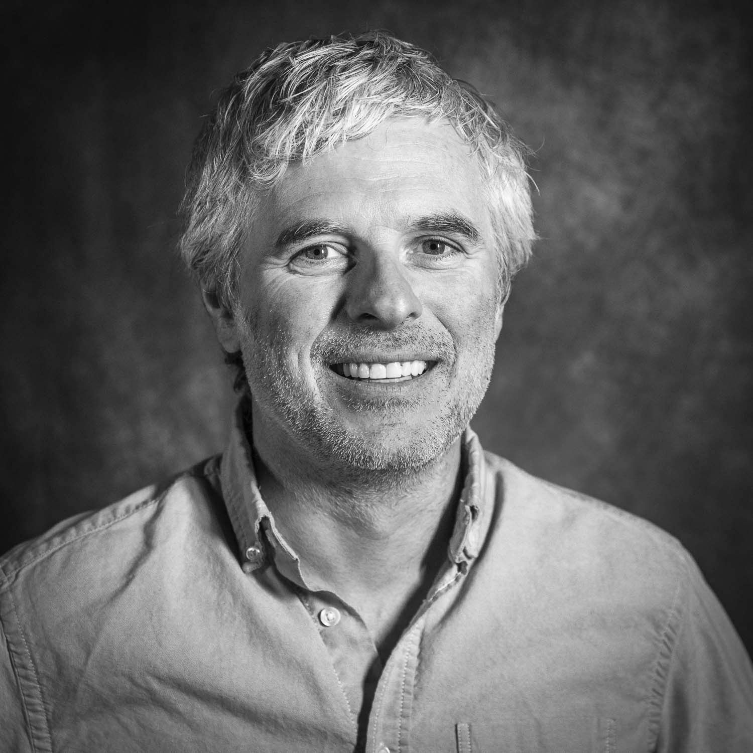 Smiling middle-aged man with gray hair in black and white portrait photo wearing casual shirt.