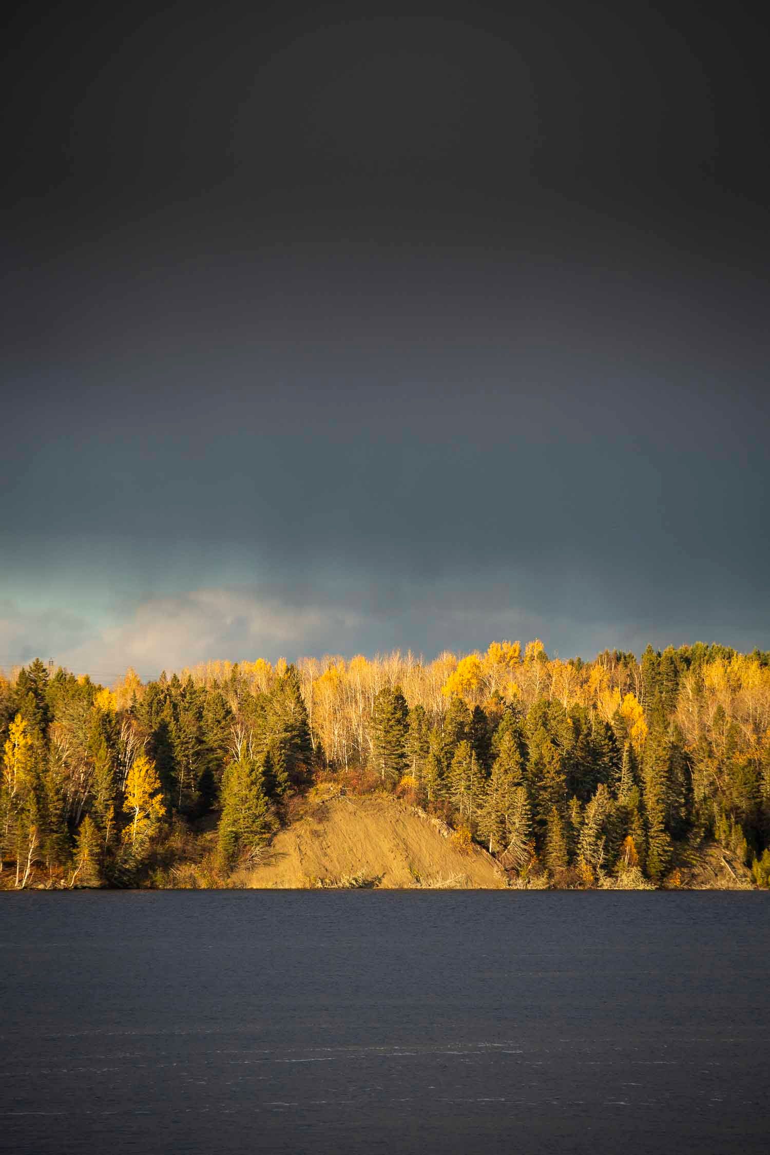 Paysage fin de journée, terrain abrupte
Autumn forest with yellow and green trees reflected on a calm lake under a dramatic dark stormy sky.