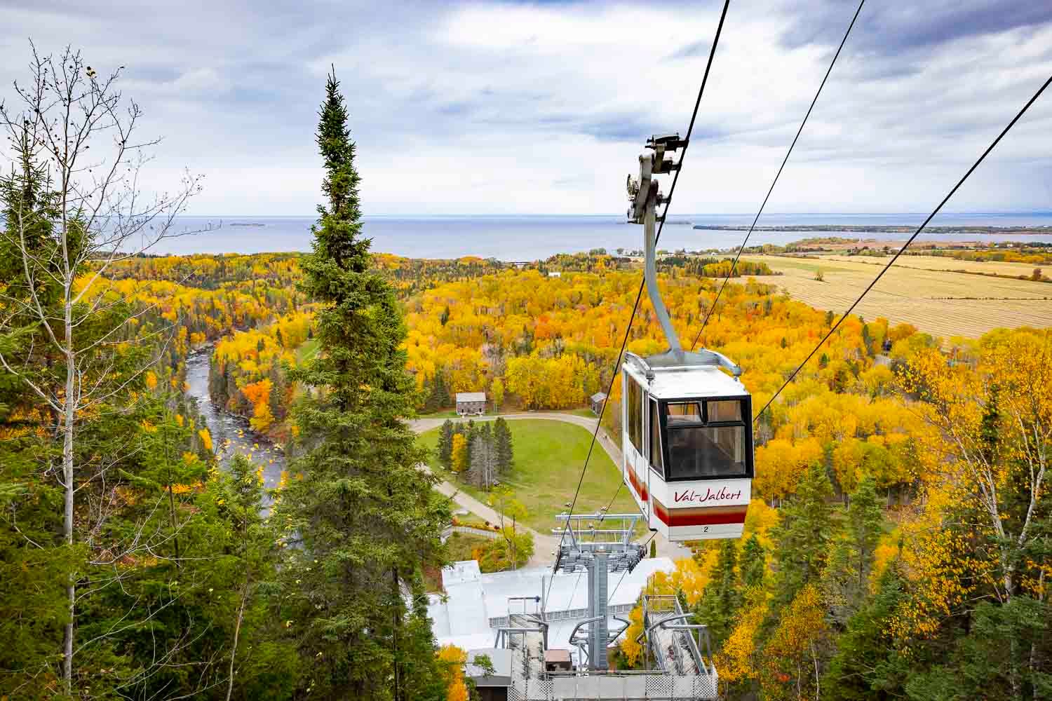 Val-Jalbert
Aerial gondola cable car descending over colorful autumn forest with yellow and green trees under cloudy sky.