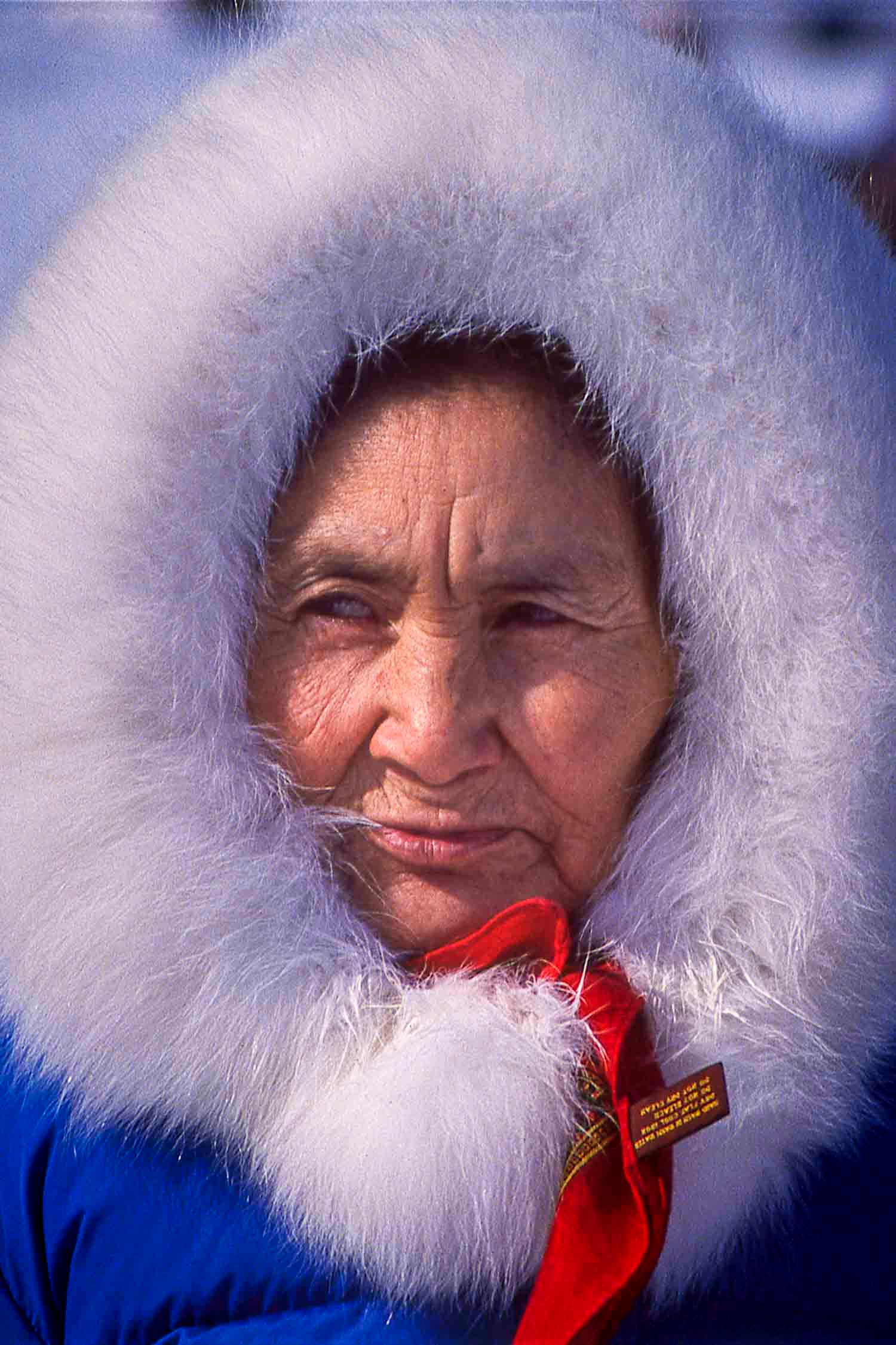 Femme inuite
Nunavik, Québec, C
Elderly Indigenous woman wearing a blue parka with white fur-trimmed hood and red scarf, outdoors in winter.