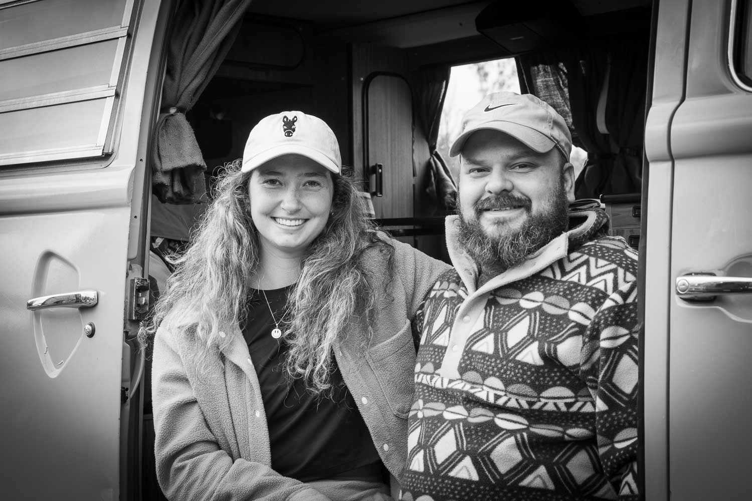 A smiling couple poses together inside a vintage van in a black and white photo.