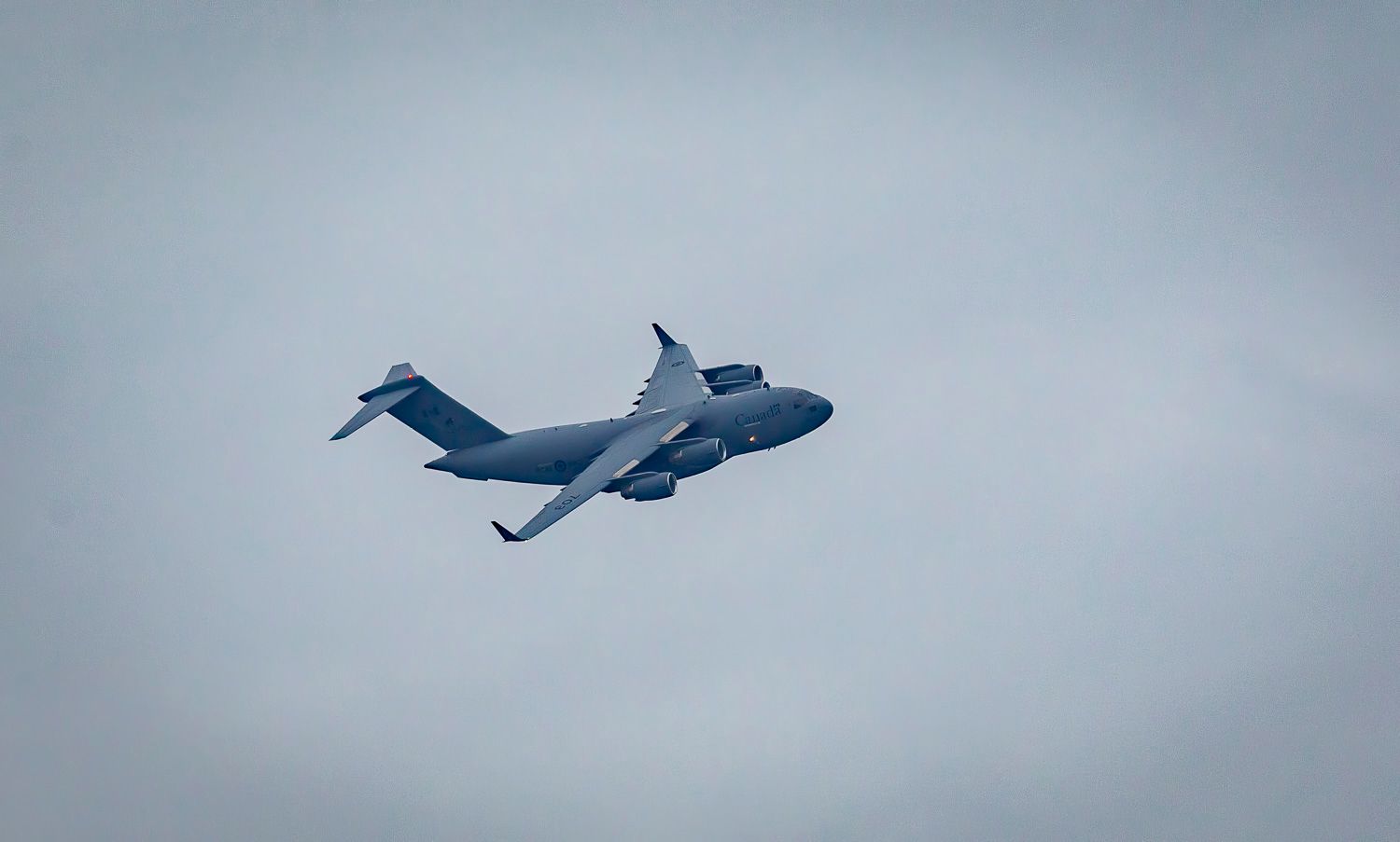 Large grey military C-17 Globemaster transport aircraft flying against an overcast grey sky.