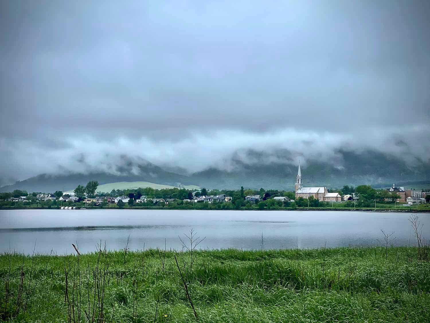 Carleton sur mer dans la brume
Québec
Misty clouds rolling over a small lakeside town with green grass in the foreground on an overcast day.