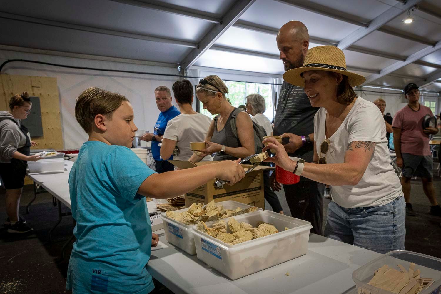 Boy and woman sharing food samples at outdoor festival serving table under tent.