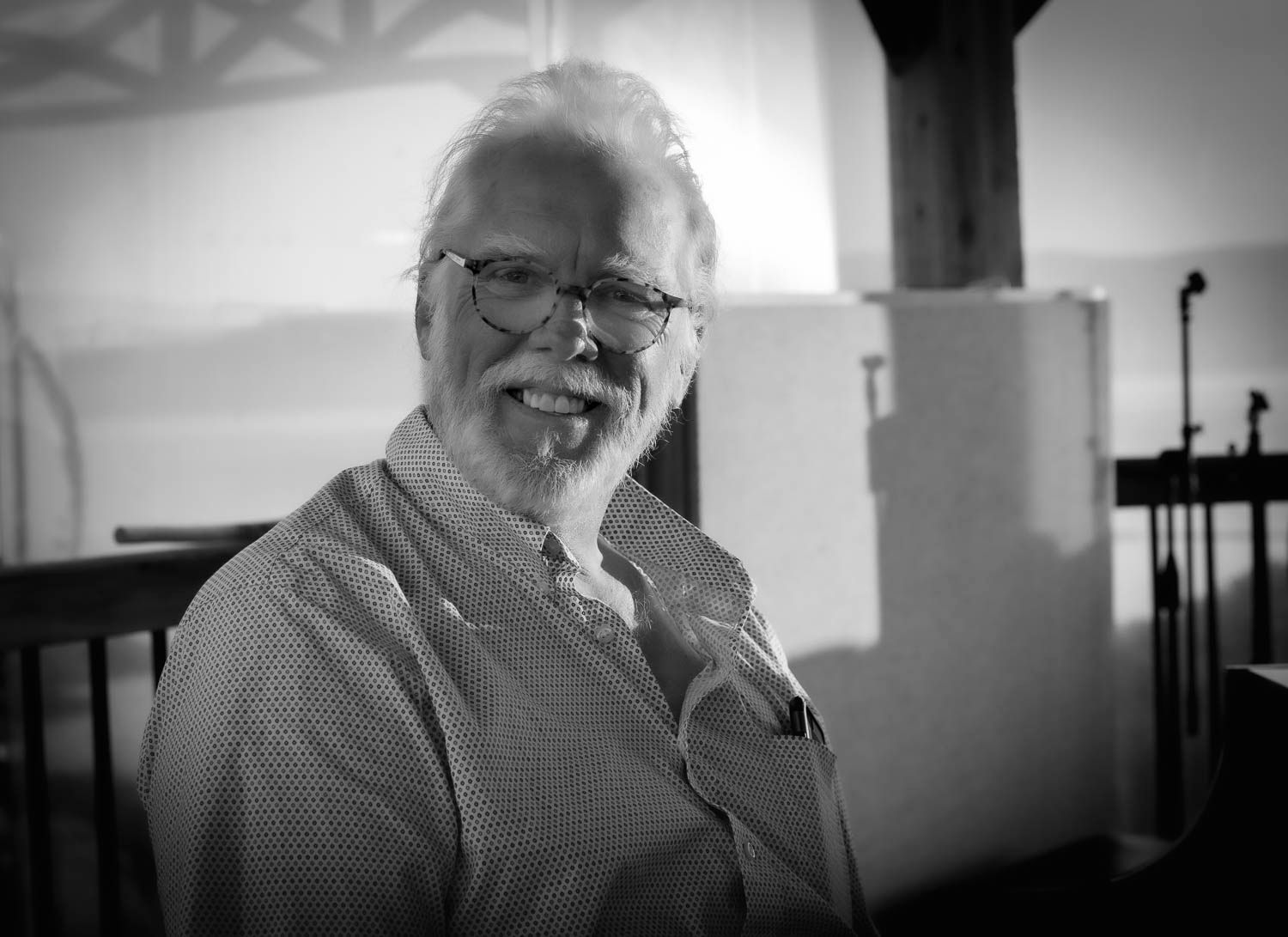 Black and white portrait of a smiling older man with white hair and beard indoors.