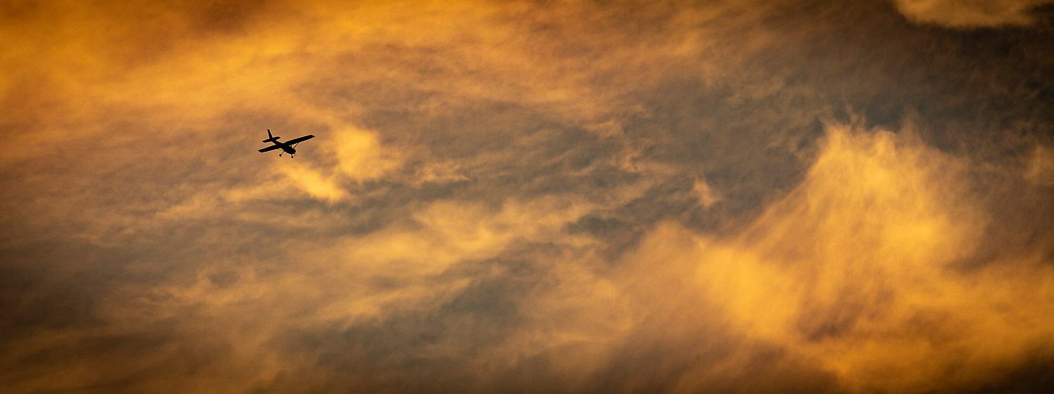 Silhouette of a small airplane flying through dramatic golden orange sunset clouds.
