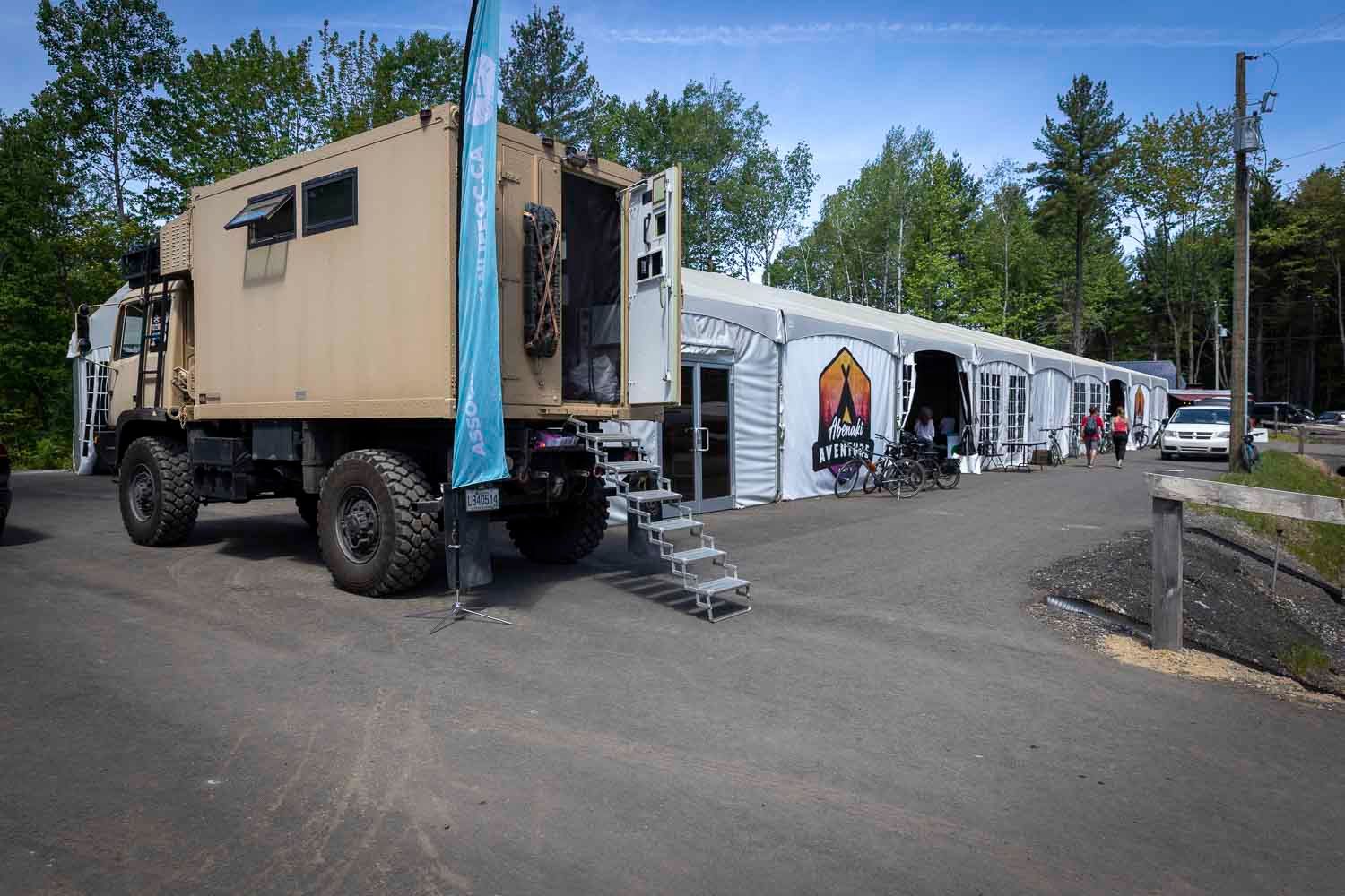 Large military-style off-road vehicle parked outside a tent event space surrounded by trees.