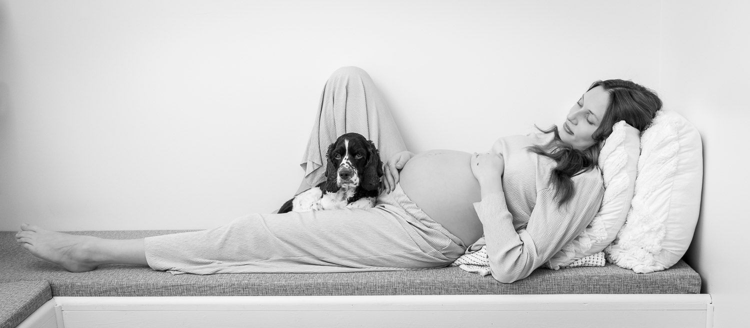 Black and white photo of a pregnant woman relaxing on a daybed with her Springer Spaniel dog.
