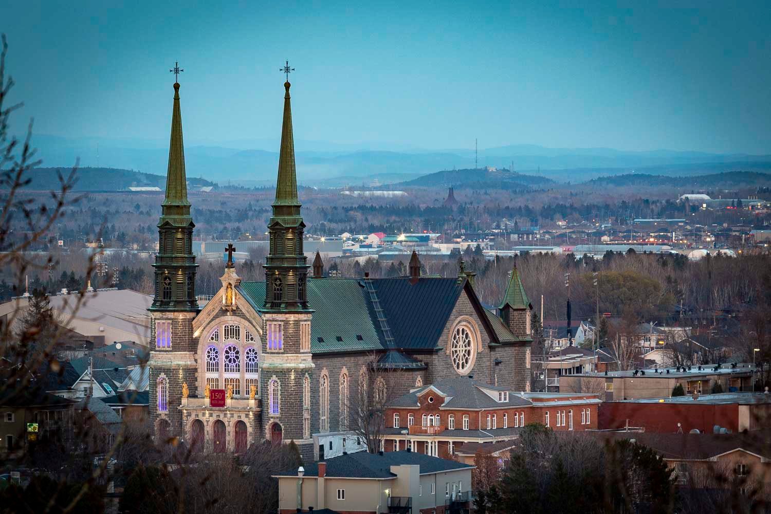Gothic church with twin spires dominates the skyline of a small city surrounded by rolling hills.
