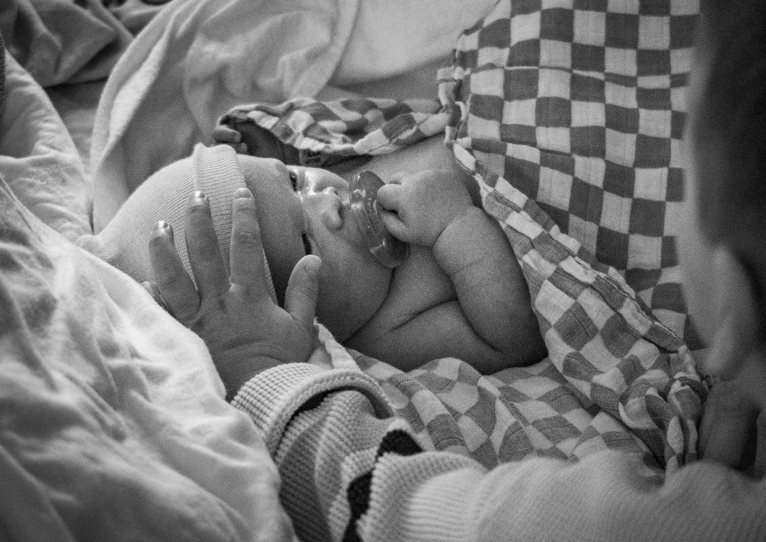 Black and white photo of a newborn baby wrapped in checkered blanket in hospital.