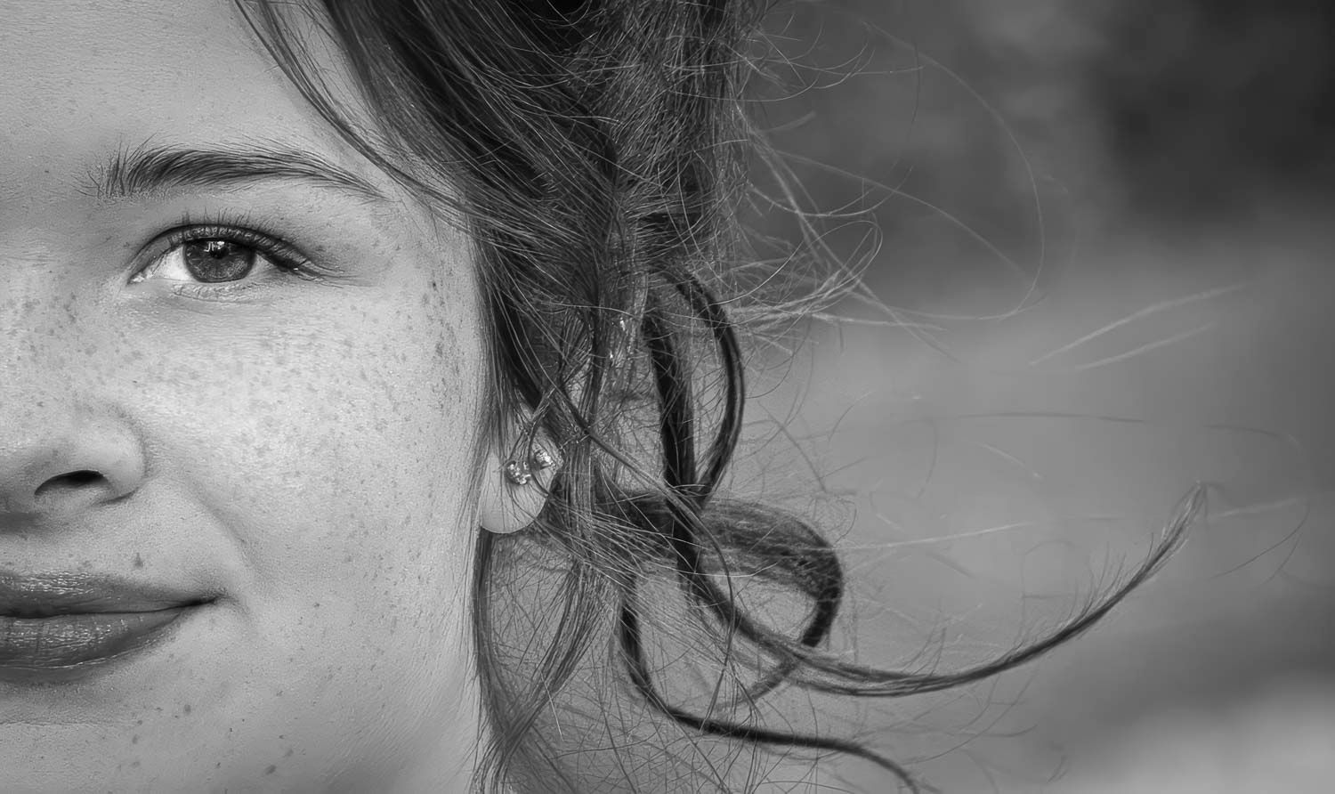 Élodie
Jeune femme, gros plan, Québec, C
Black and white close-up portrait of a young girl with freckles and windswept hair, smiling softly.
