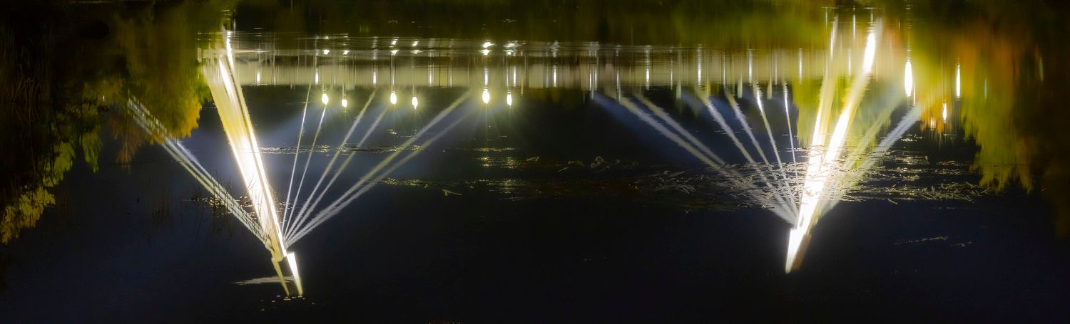 Spectacular water fountain light show reflecting on a dark lake surface at night.