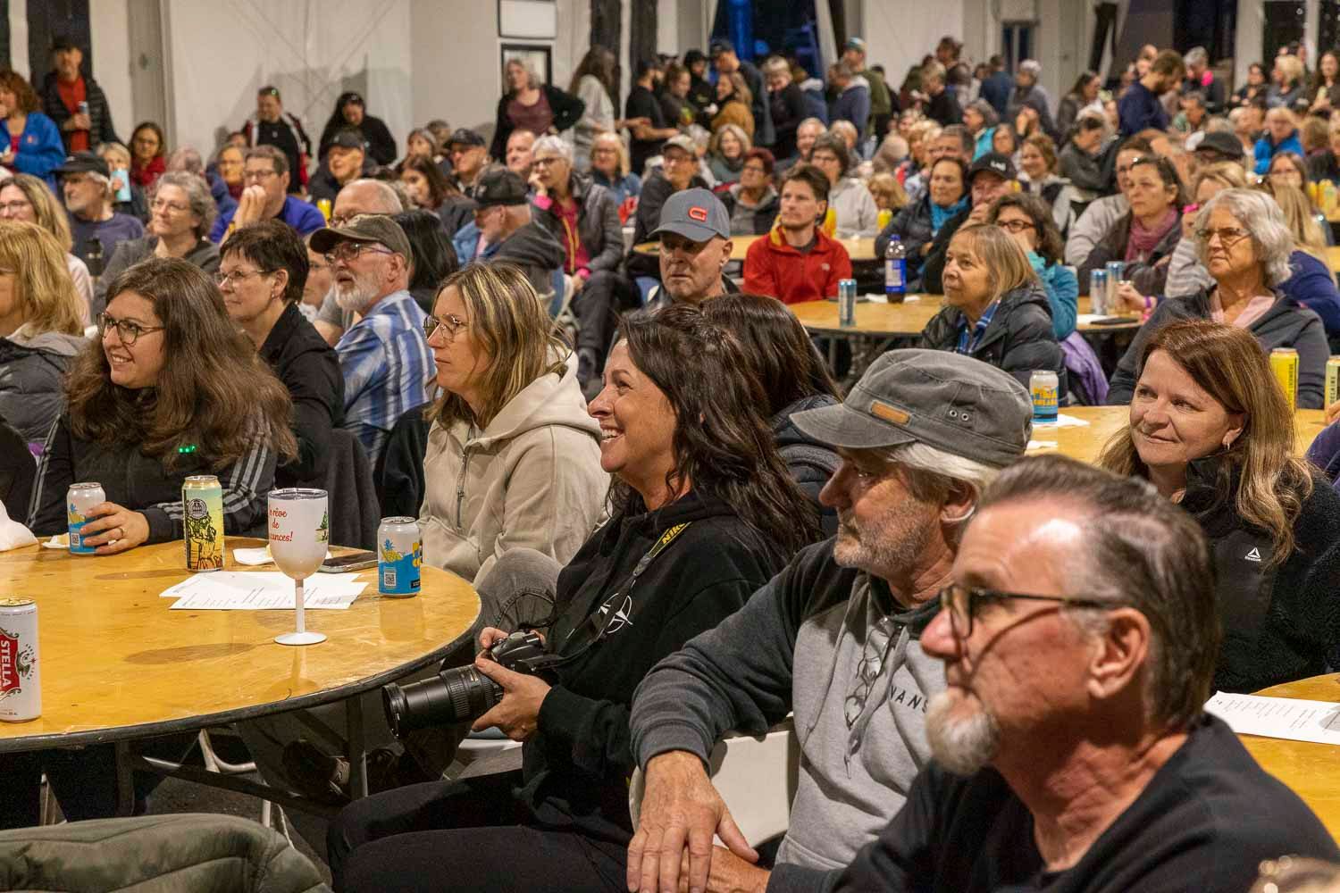 Large crowd of adults seated at round tables during an indoor community event or meeting.