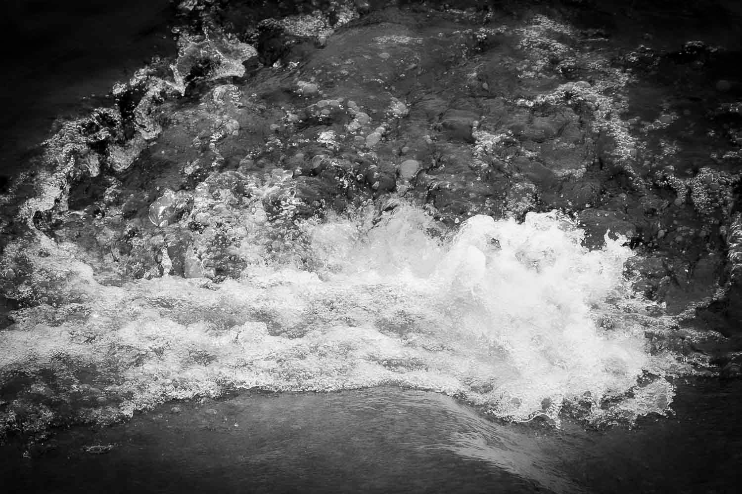 Black and white photo of rushing white water rapids flowing over dark rocks.