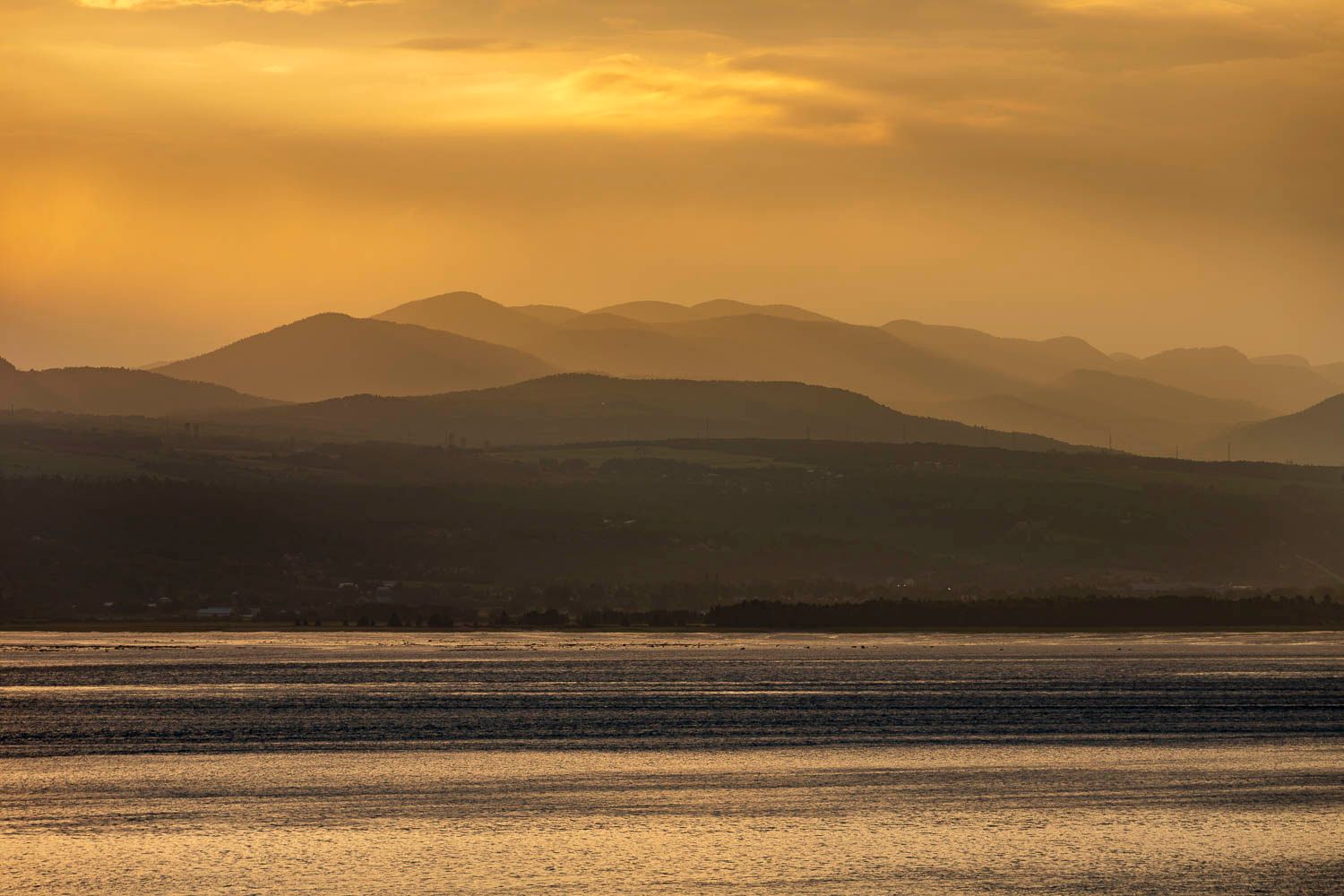 Layered mountain silhouettes bathed in warm golden sunset light reflecting over tranquil water.