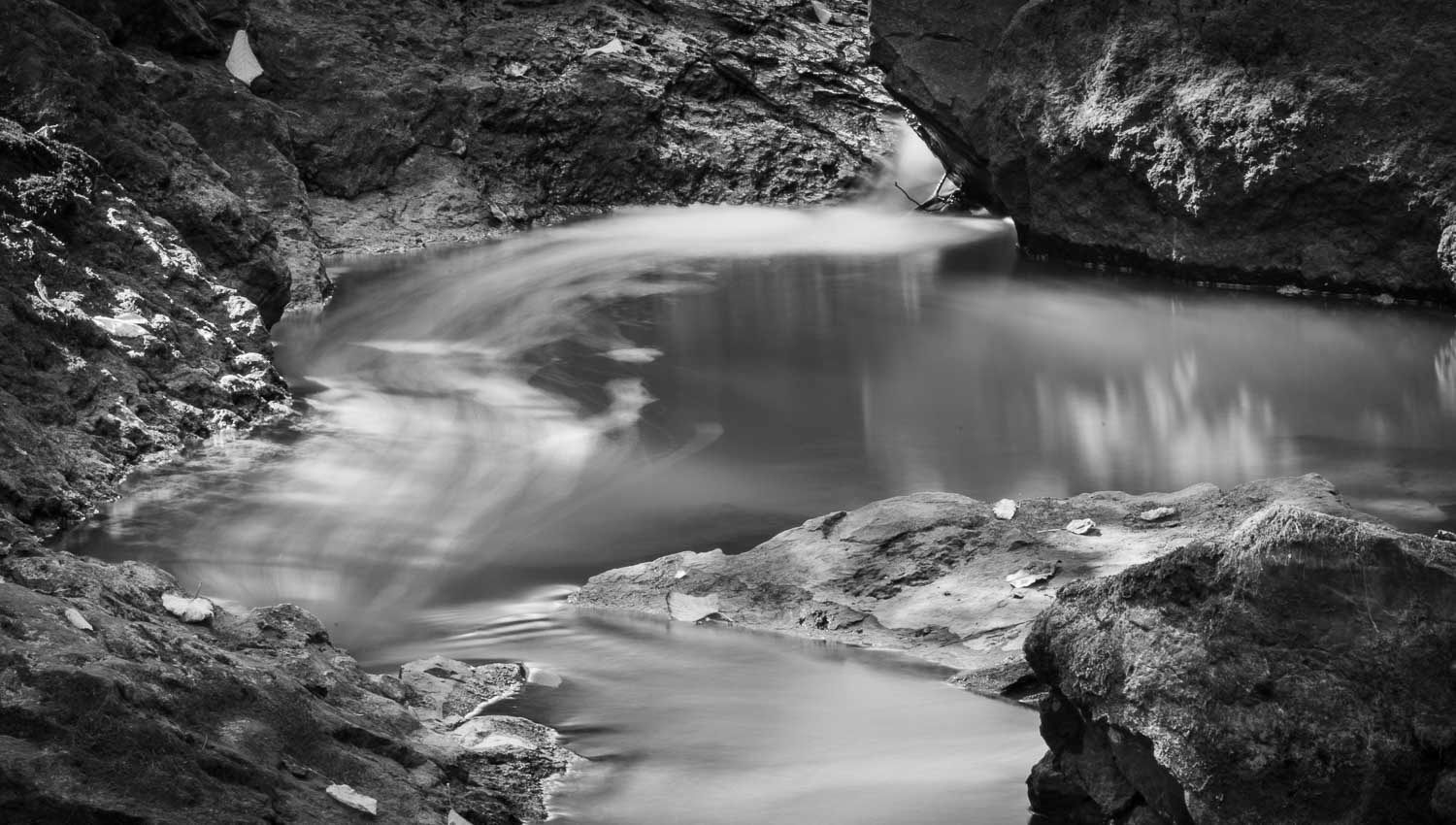 Black and white long exposure photograph of smooth flowing water through rocky canyon gorge in nature.