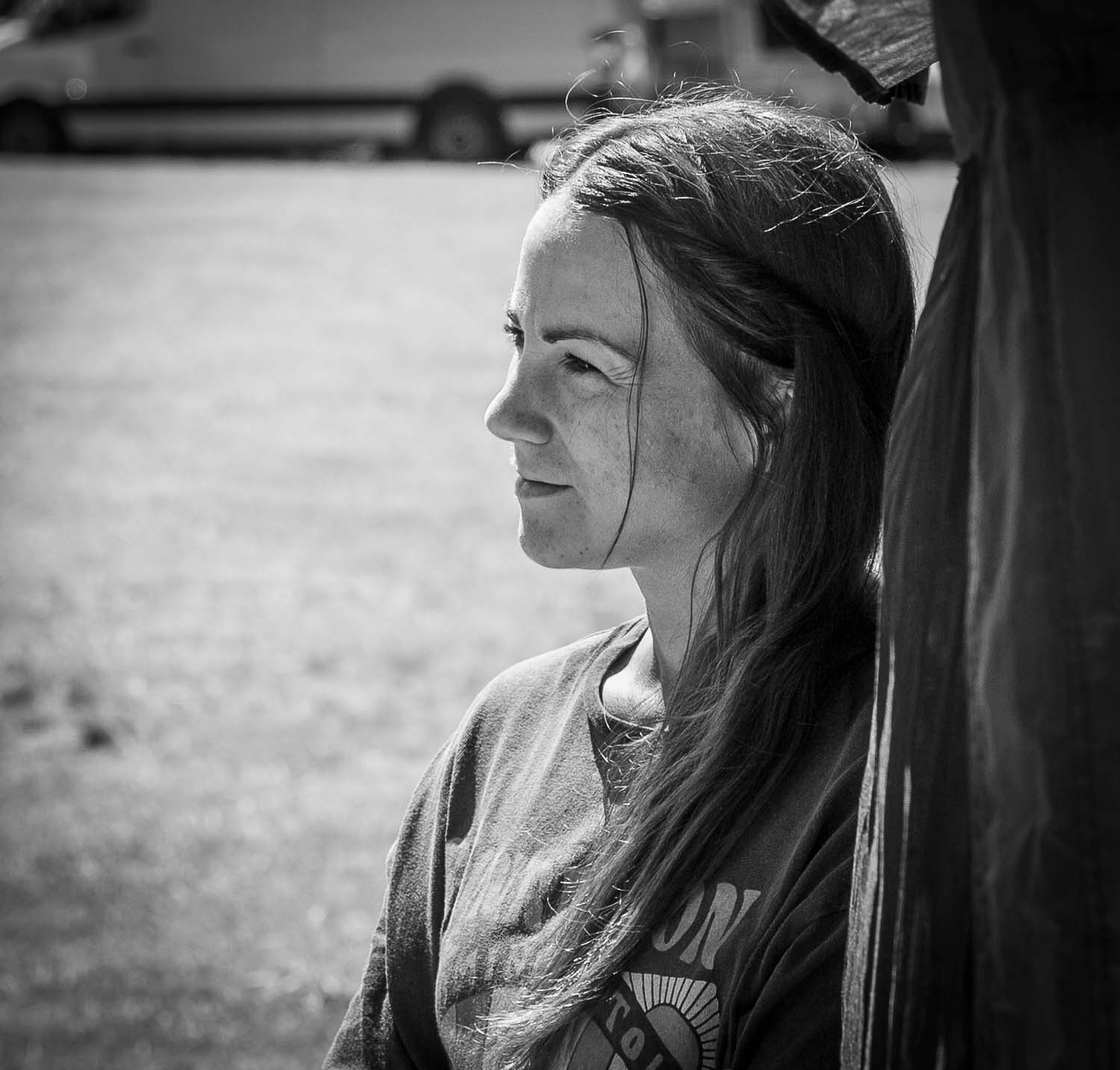 Black and white profile portrait of a young woman with long hair leaning against a post outdoors.