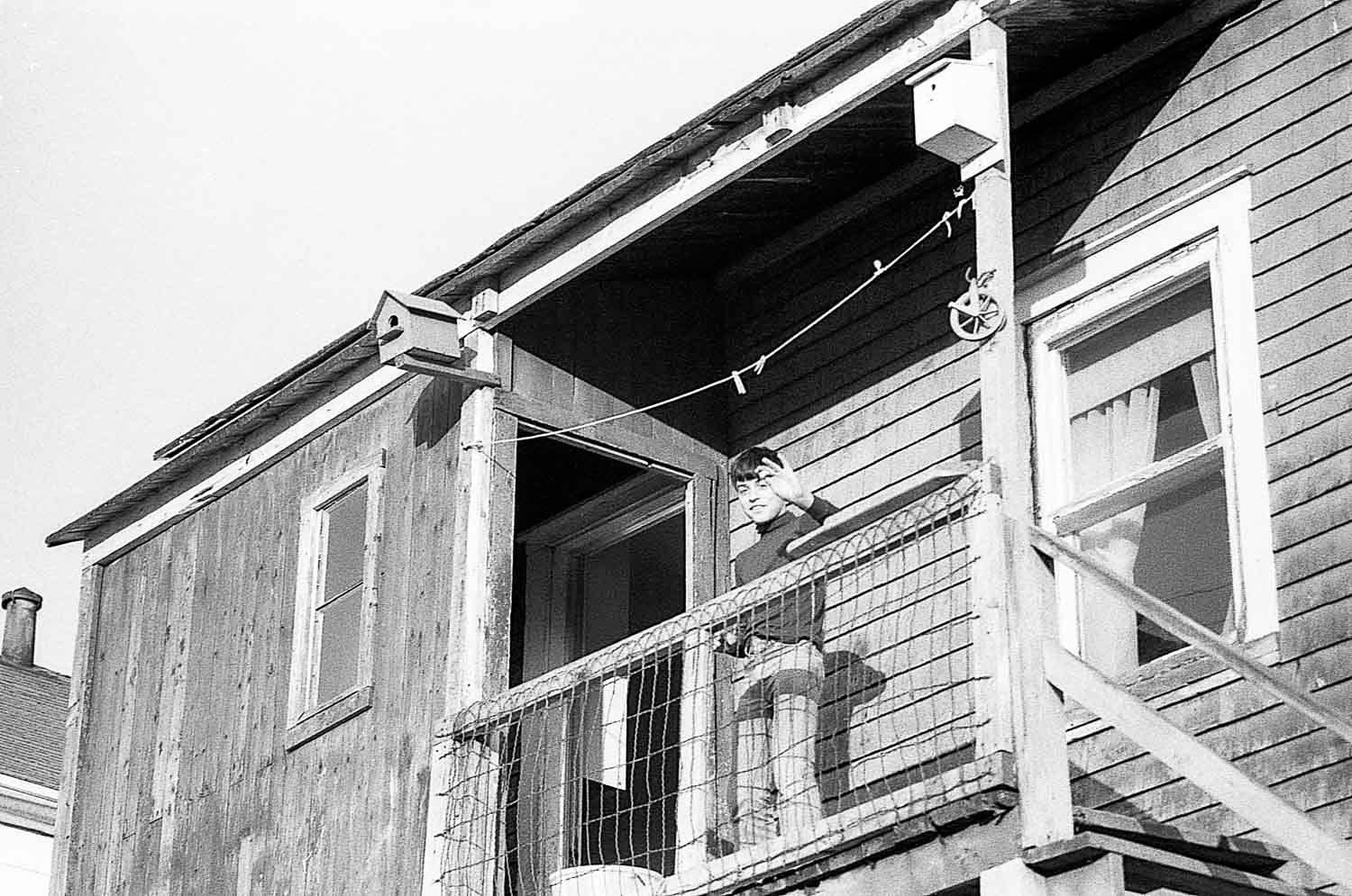 Black and white photo of a weathered wooden building exterior with a second-floor balcony and clothesline.