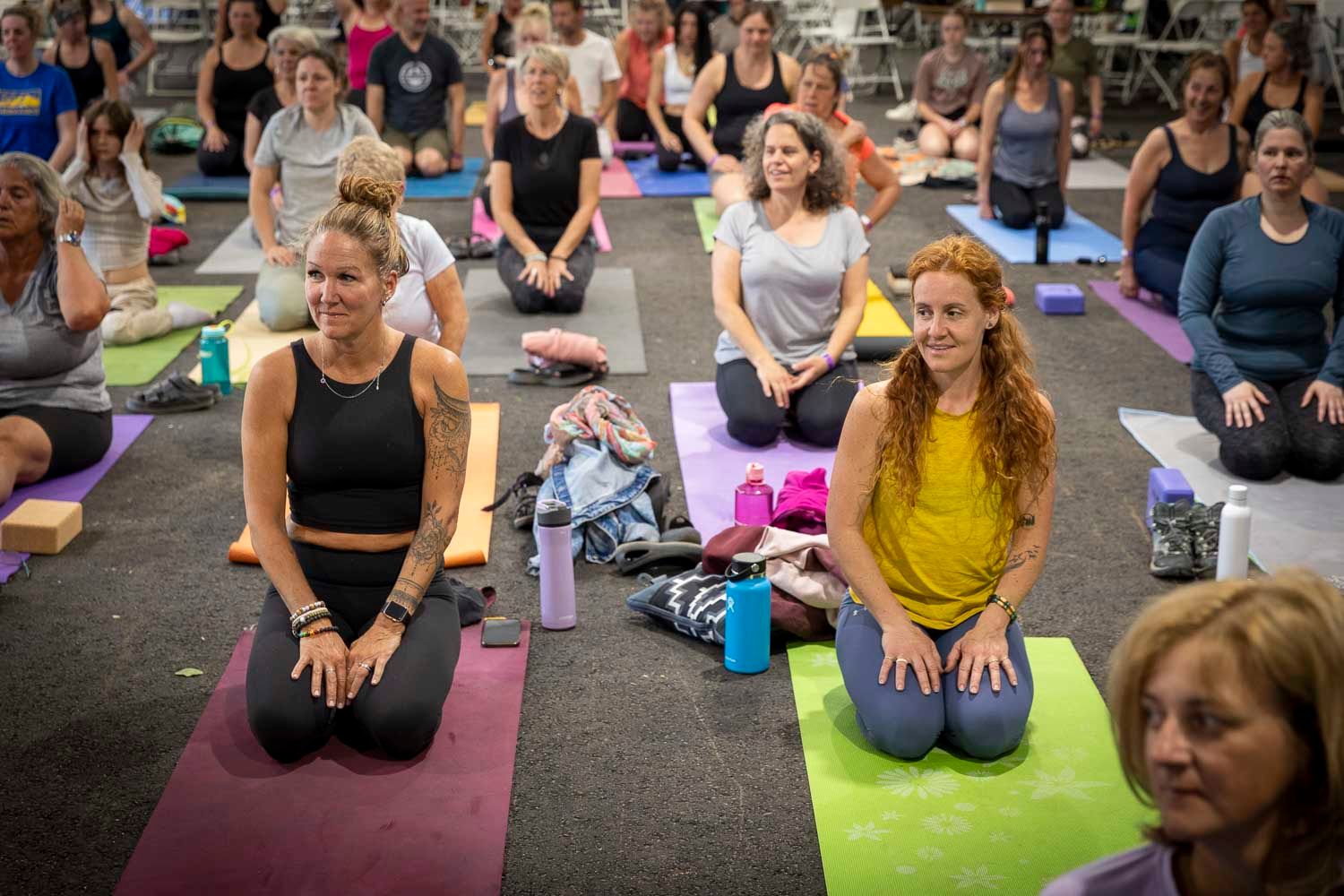 Group of women practicing yoga on colorful mats in a large indoor fitness studio.