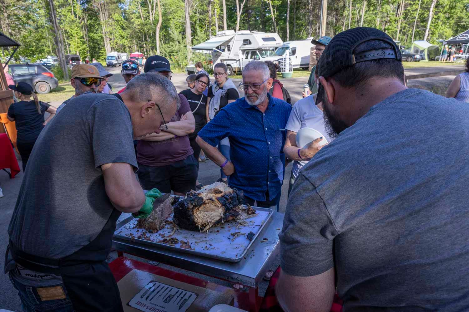 Group of men carving and serving smoked BBQ meat at outdoor food festival.